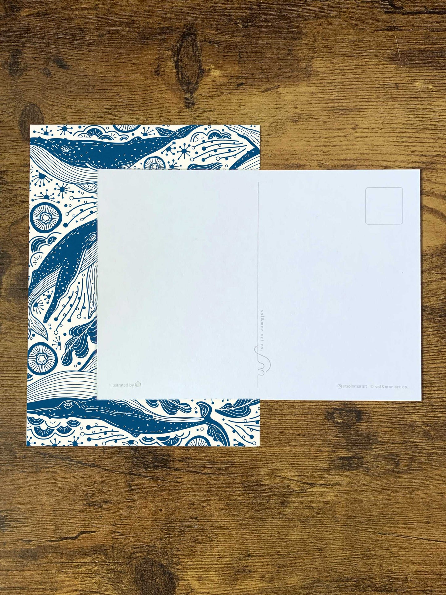 Whale and ocean art postcard with blue design on wood background.