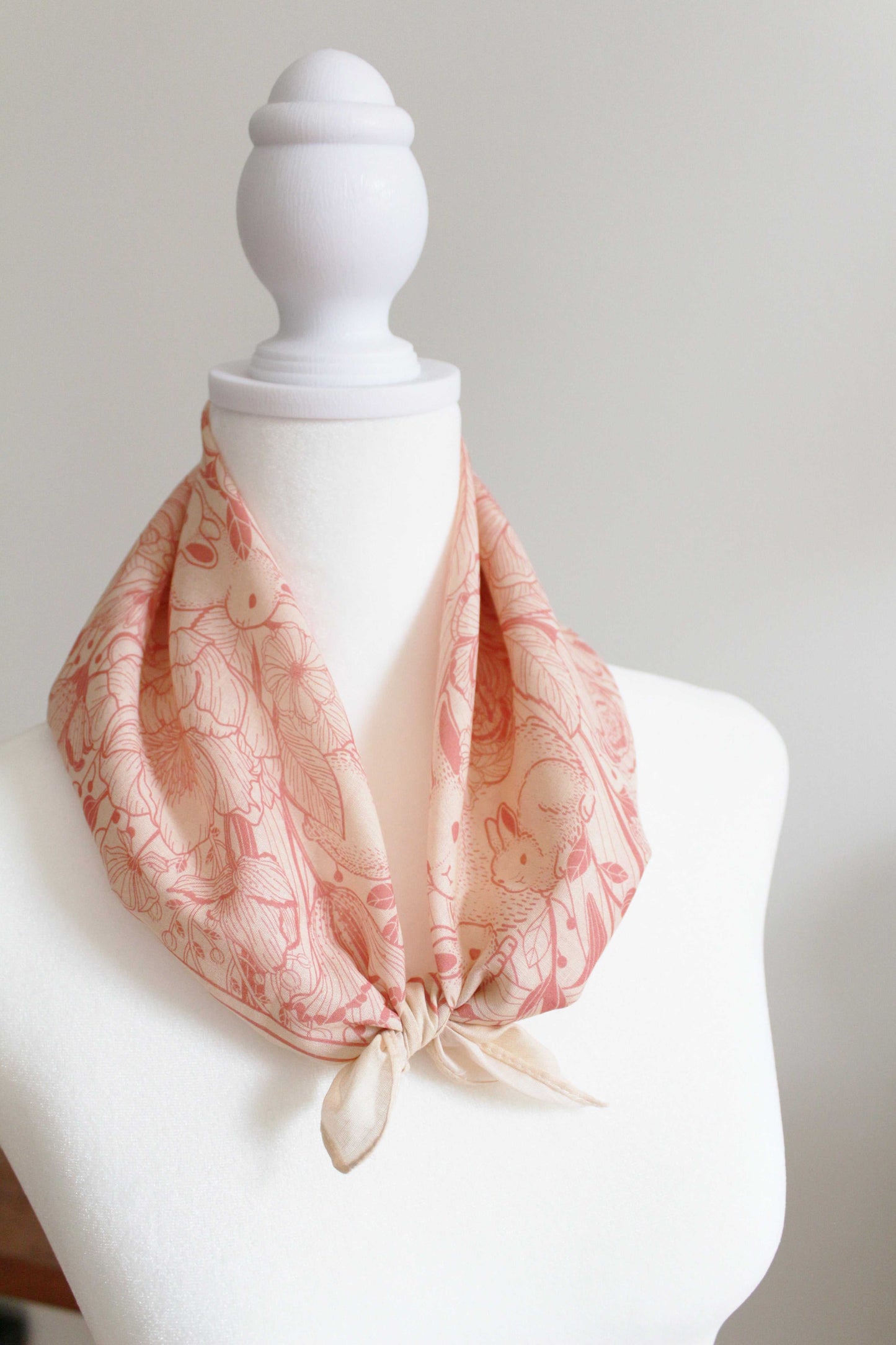 Pastel pink Bunny in the Floral Breeze Bandana Scarf displayed on a mannequin, showcasing its soft cotton fabric and floral design.