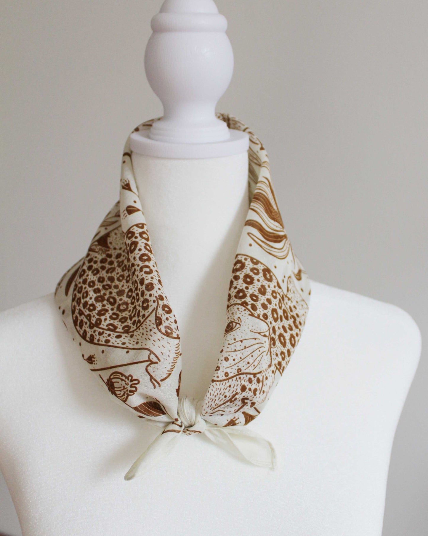 Leopard and the Sun off-white bandana scarf tied around a mannequin's neck showcasing artistic leopard design.