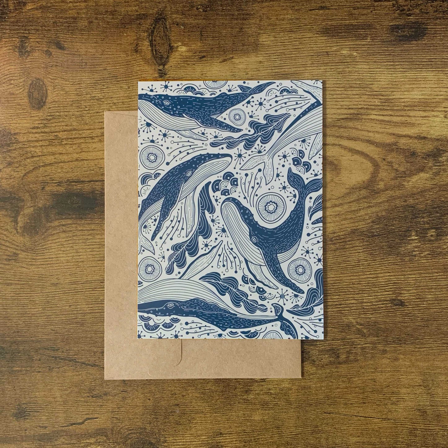 Humpback whale illustration on a patterned card against a brown kraft paper envelope.
