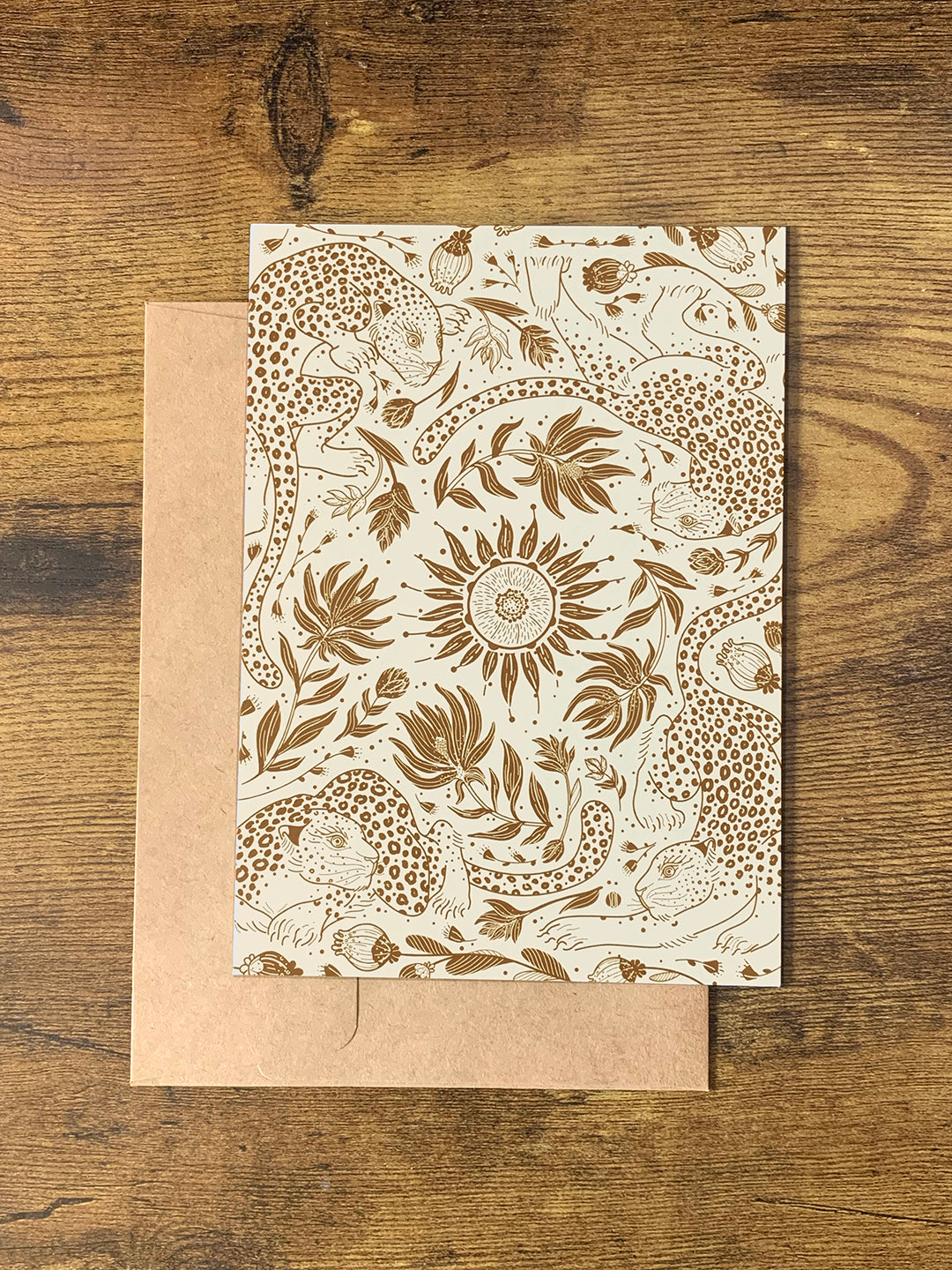Patterned card featuring leopards and flowers on a wood background with a brown envelope beneath.