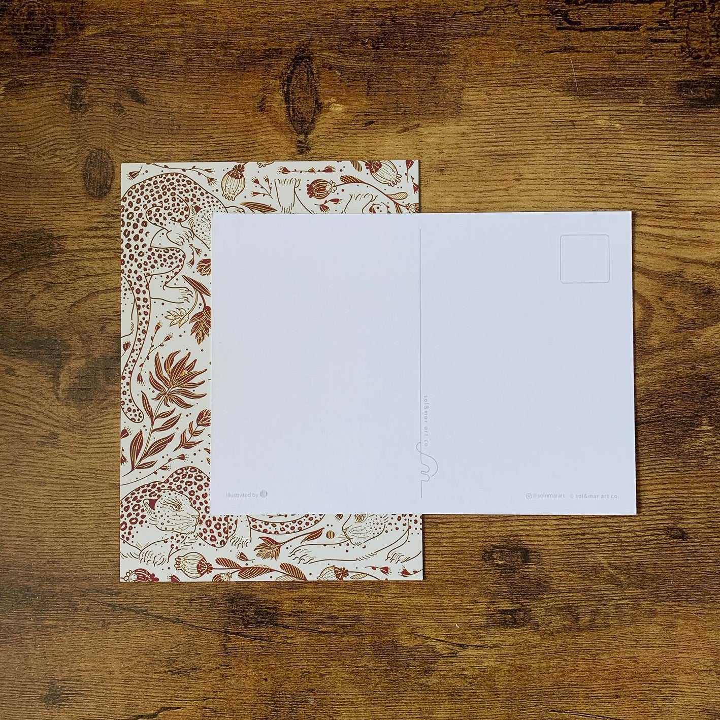 Leopard and floral patterned postcard on wooden table, featuring a blank side for writing.