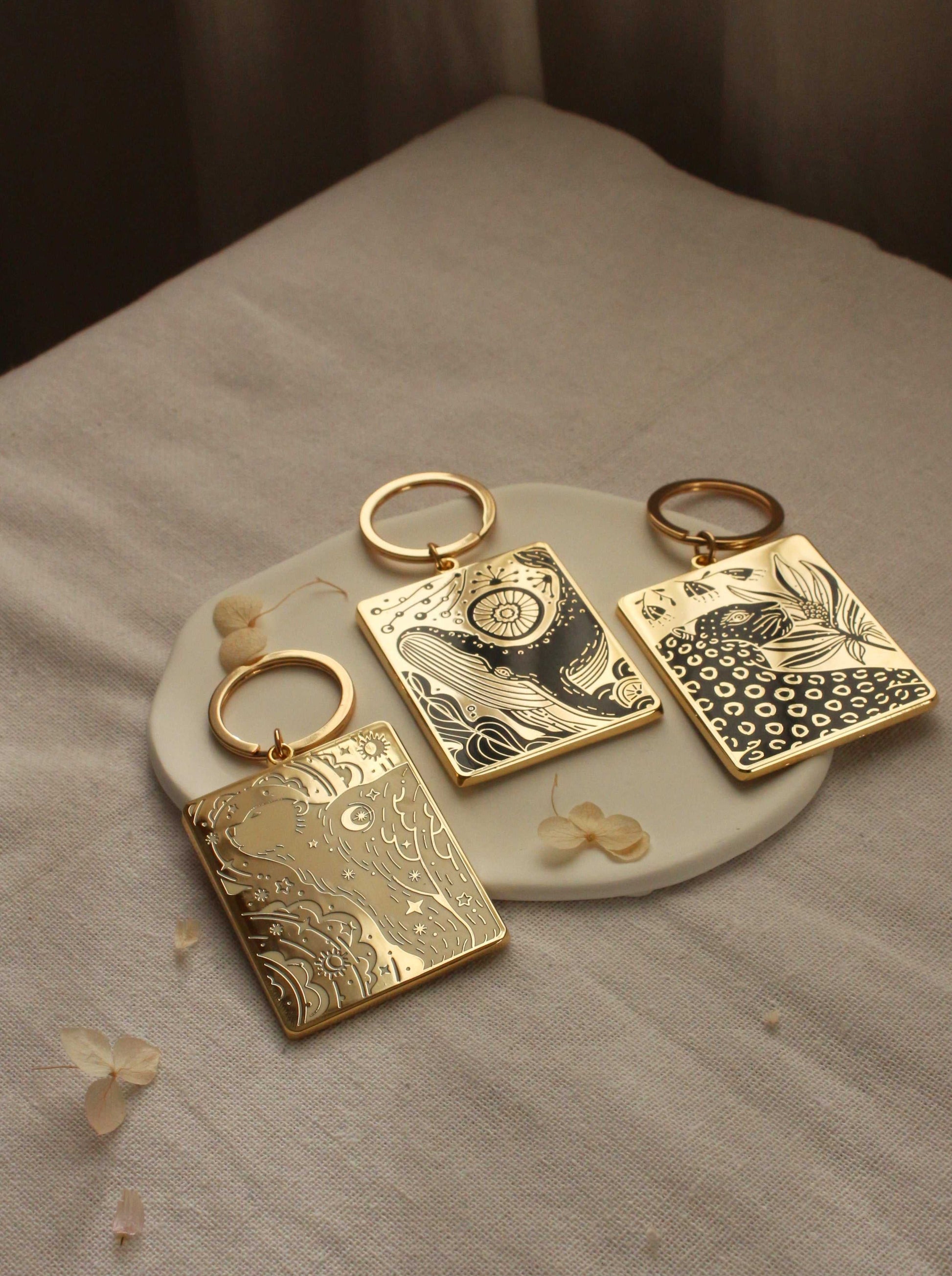 Gold plated enamel keychains with artistic designs displayed on a ceramic dish, featuring unique patterns and textures.