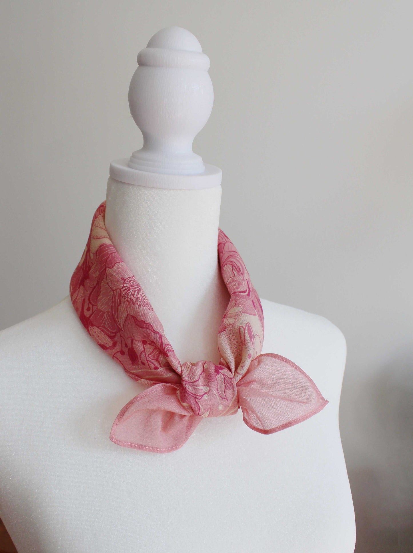 Pink bandana scarf featuring rabbits and floral patterns, styled on a mannequin for fashion display.
