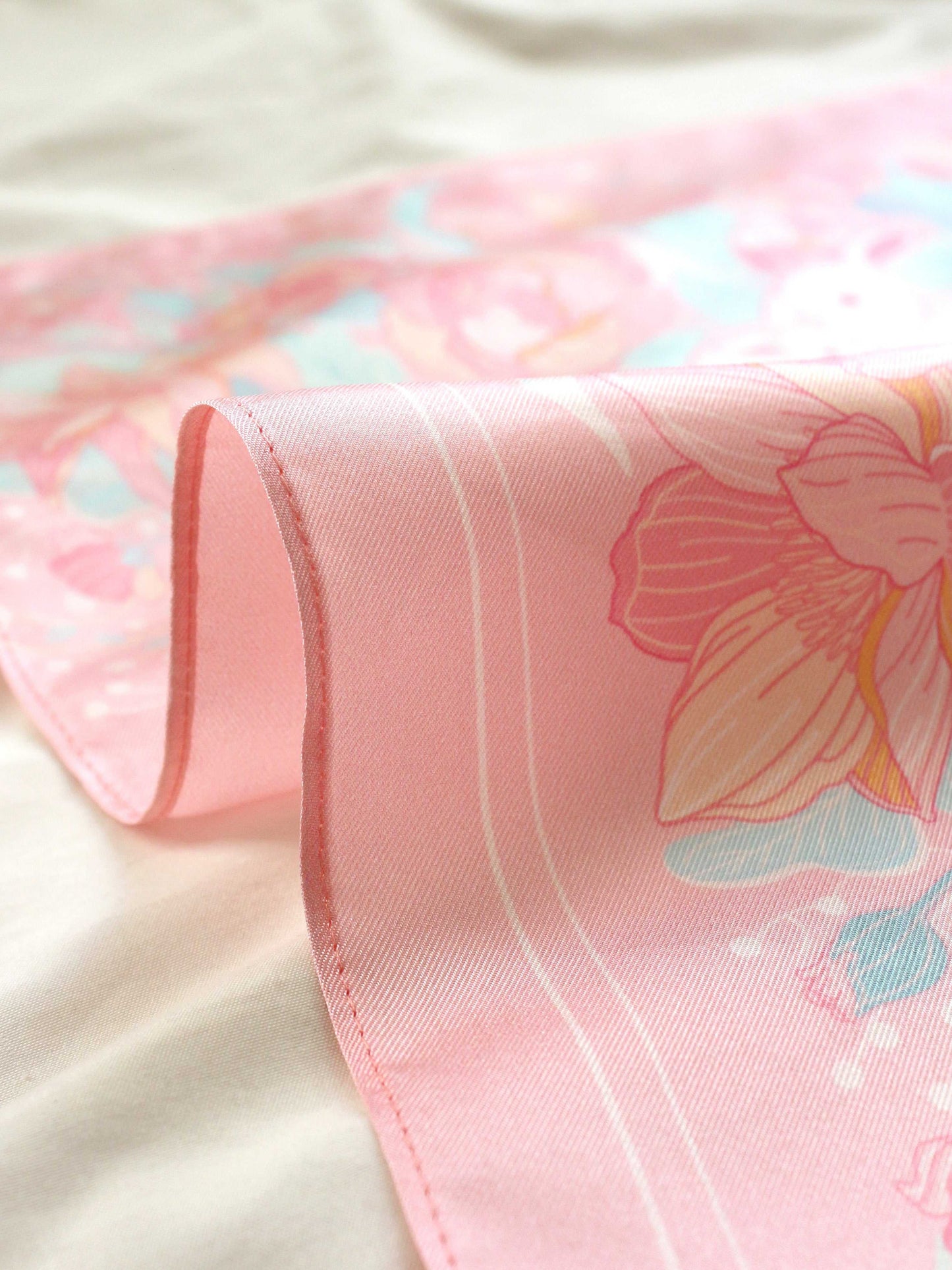 Close-up of a pink silk twill scarf featuring floral designs, showcasing softness and elegant colors.