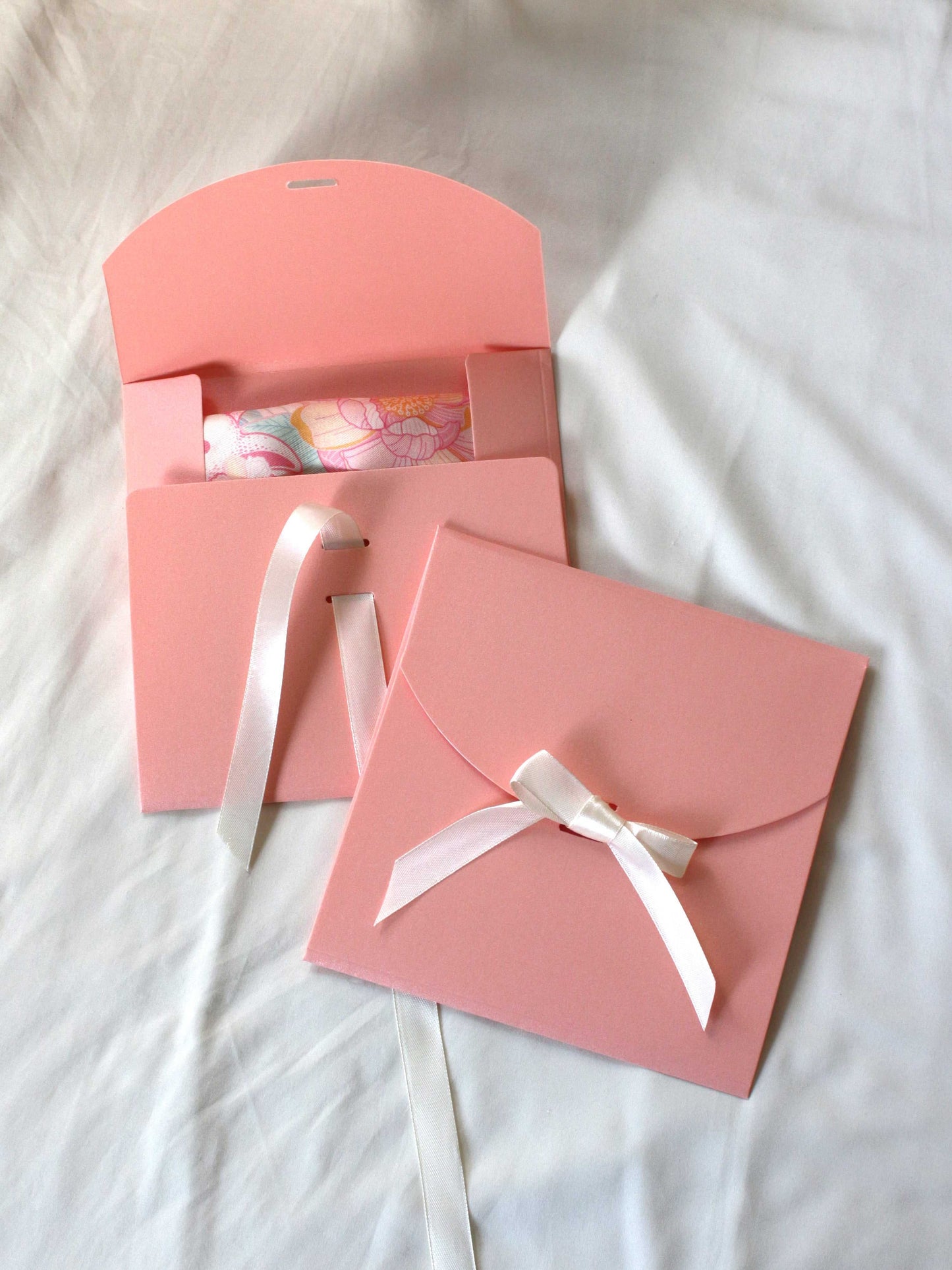 Pink gift envelopes with ribbons unveiling a colorful silk scarf inside.
