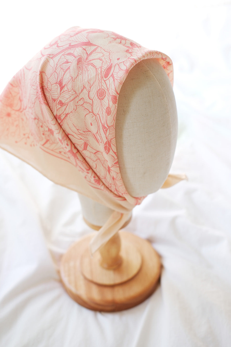 Bunny in the Floral Breeze Bandana Scarf in pastel pink displayed on a wooden stand for stylish accessory inspiration.