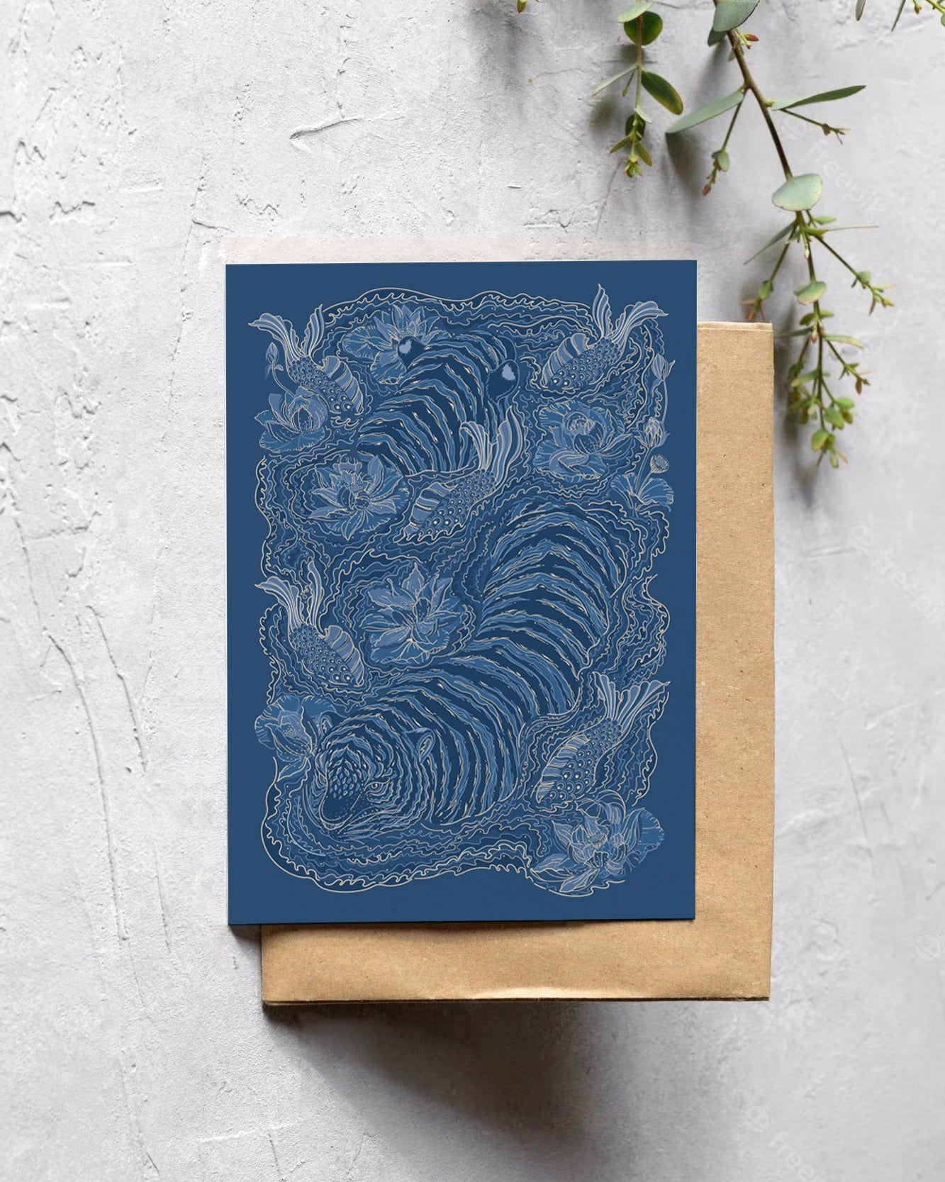 Blue greeting card with intricate design on a textured surface with greenery.