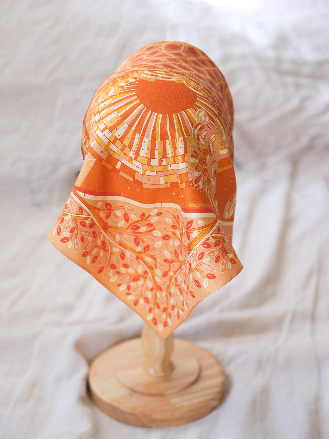 Decorative head with orange and white pattern on a wooden stand against a white background