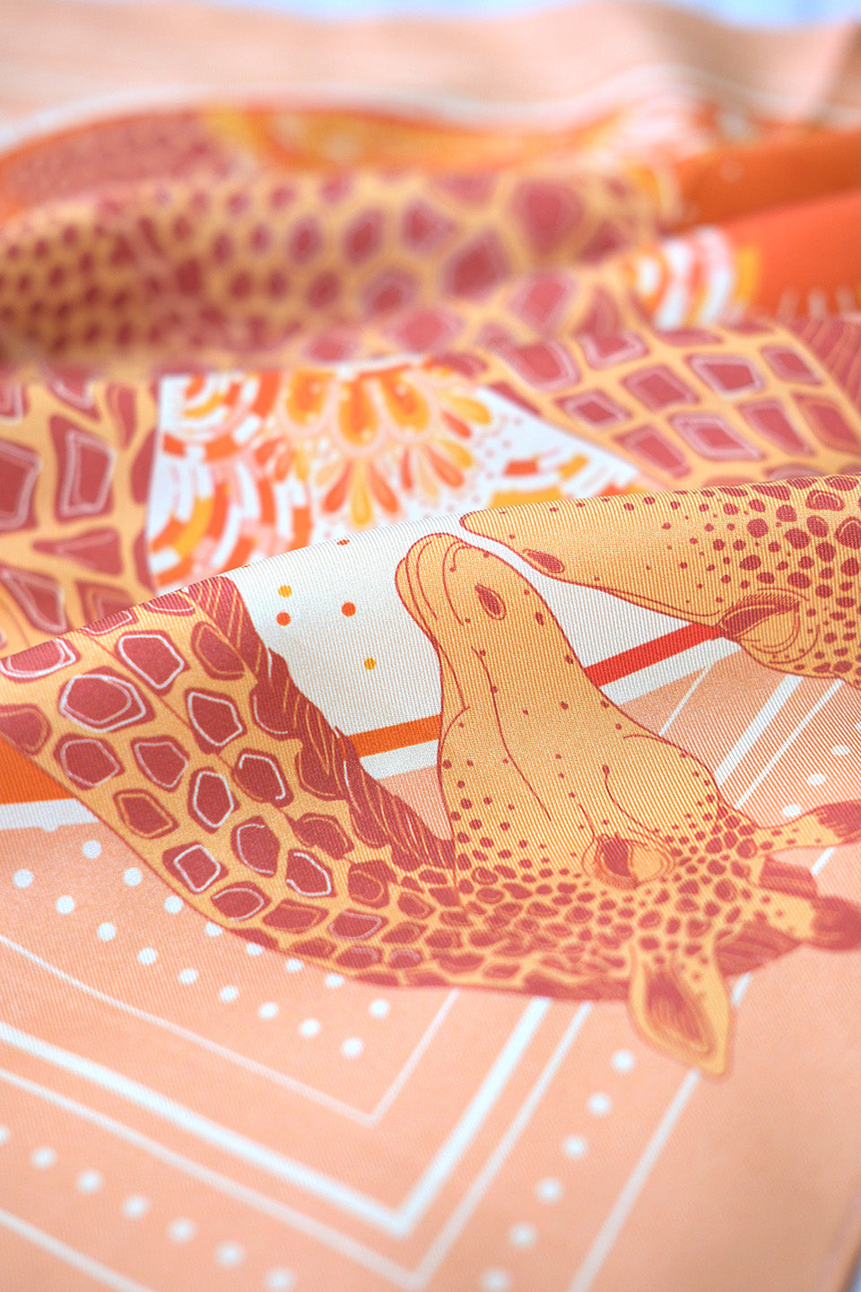 Close-up of a patterned silk scarf with giraffe design on an orange background