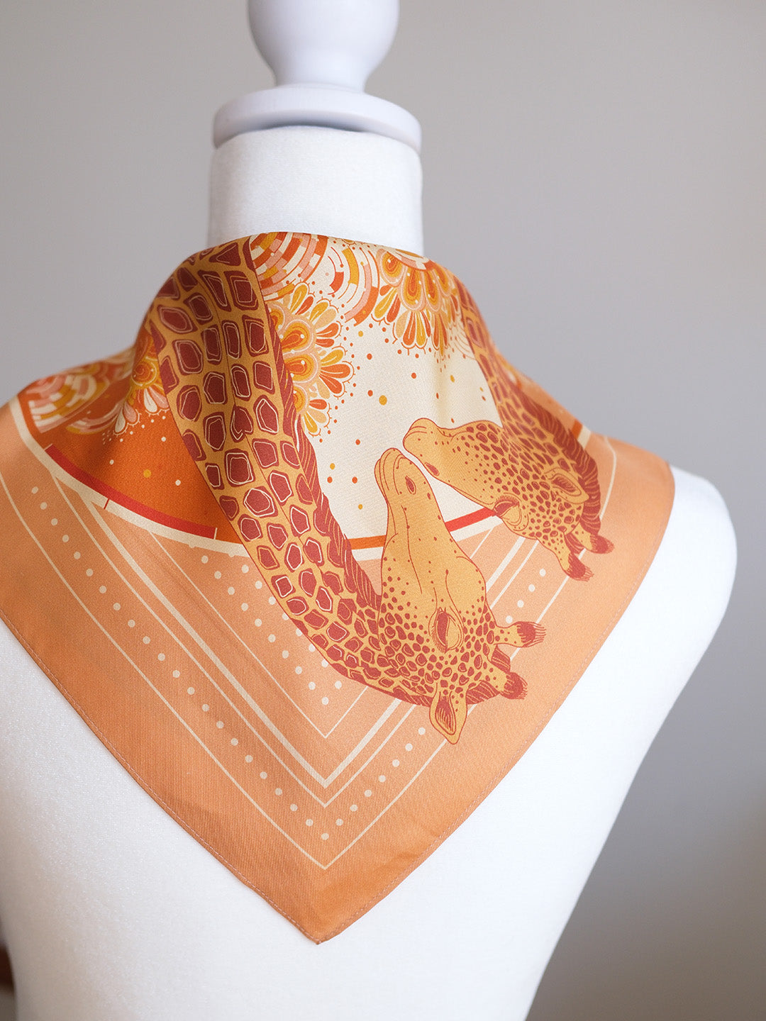 Orange scarf with giraffe pattern on a mannequin against a gray background