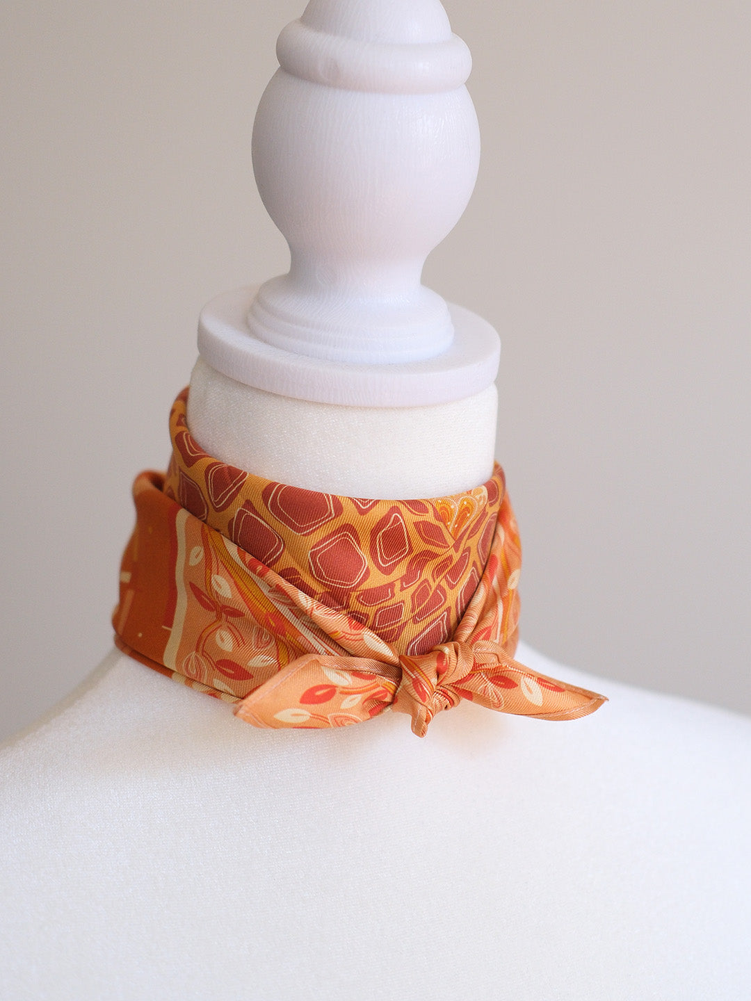 Orange giraffe patterned scarf tied around a mannequin neck against a plain background