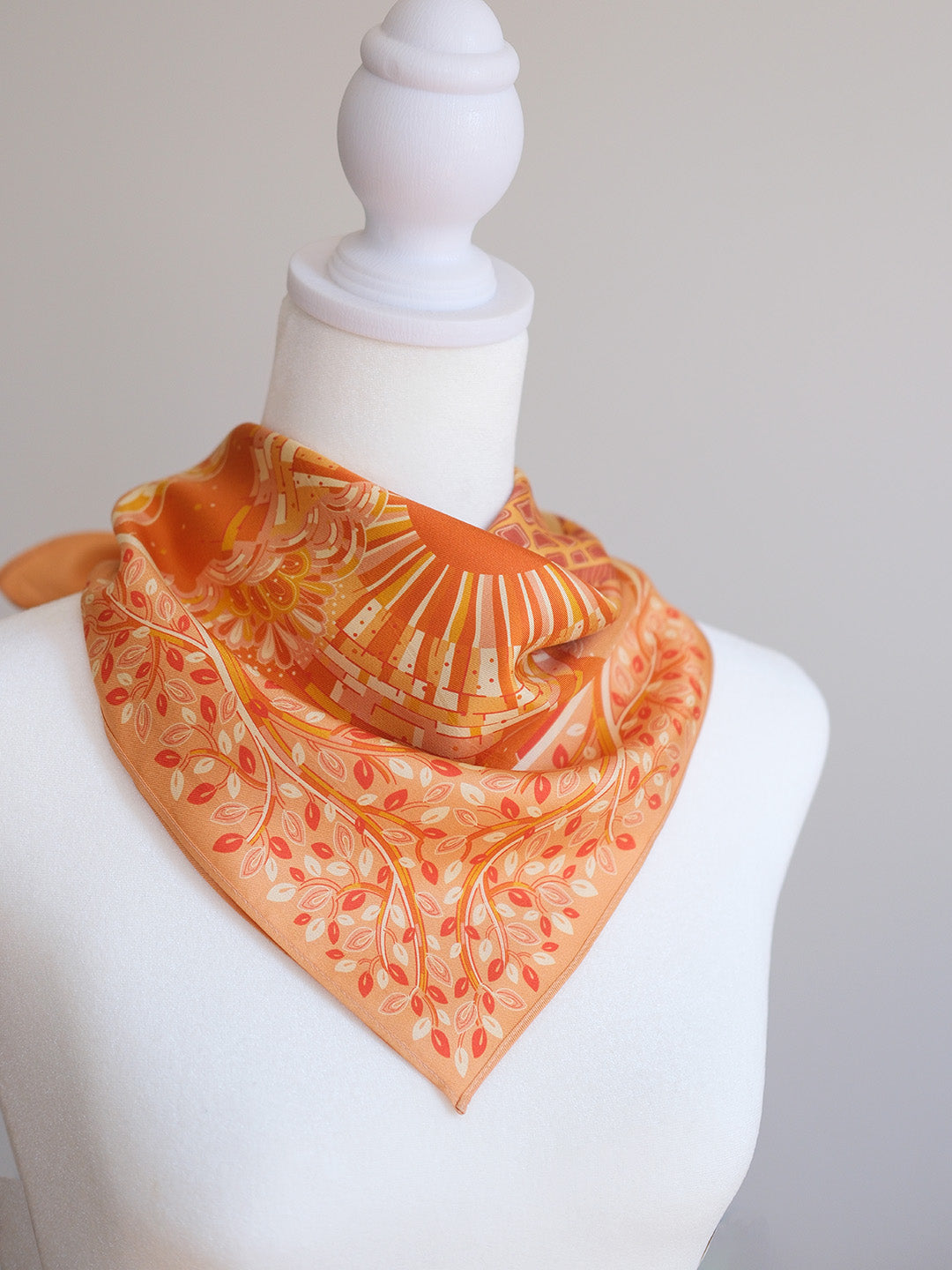Orange scarf with leaf pattern on a mannequin against a plain background