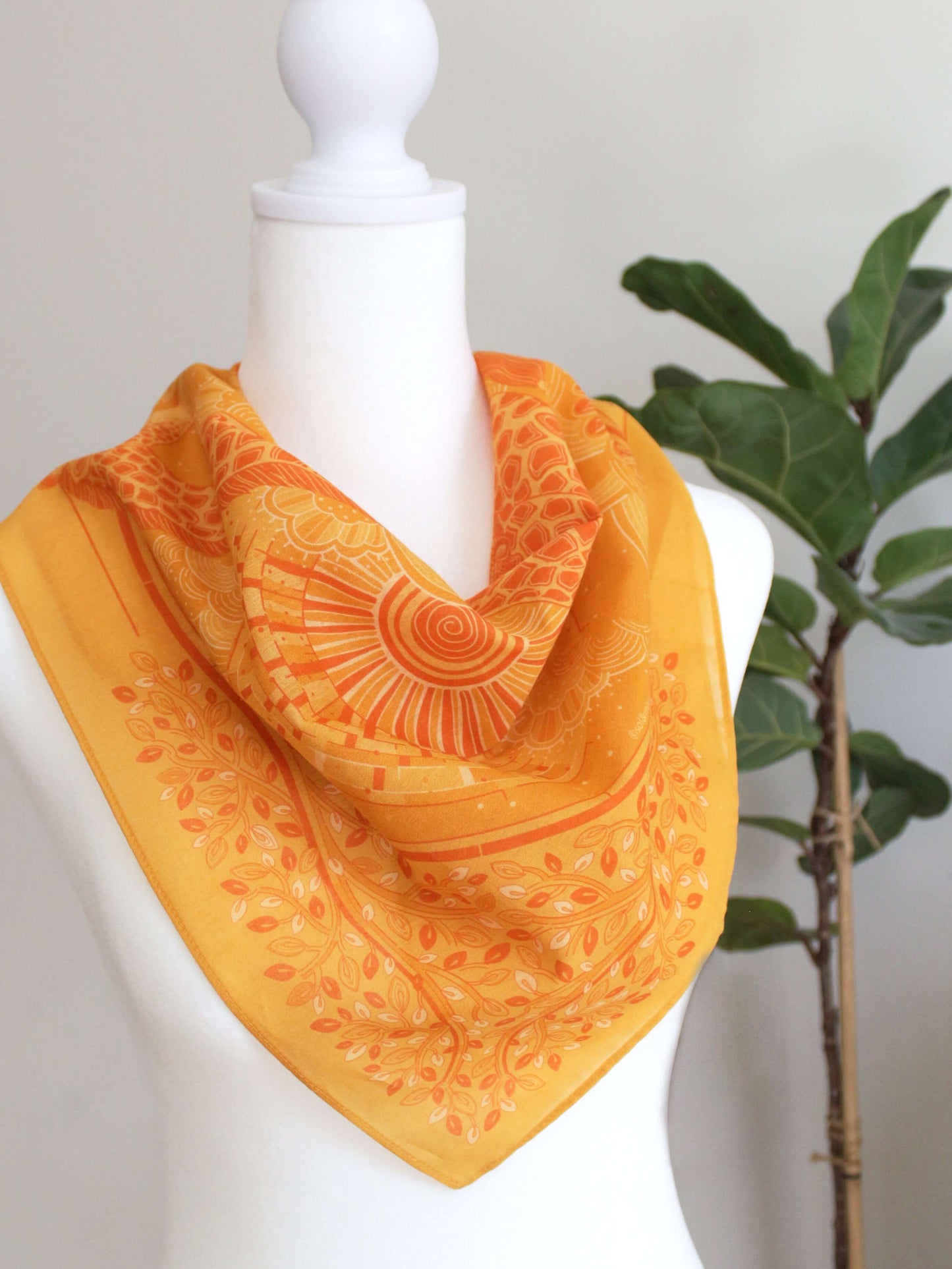 Golden yellow bandana scarf styled on a mannequin with vibrant sun and leaf patterns.