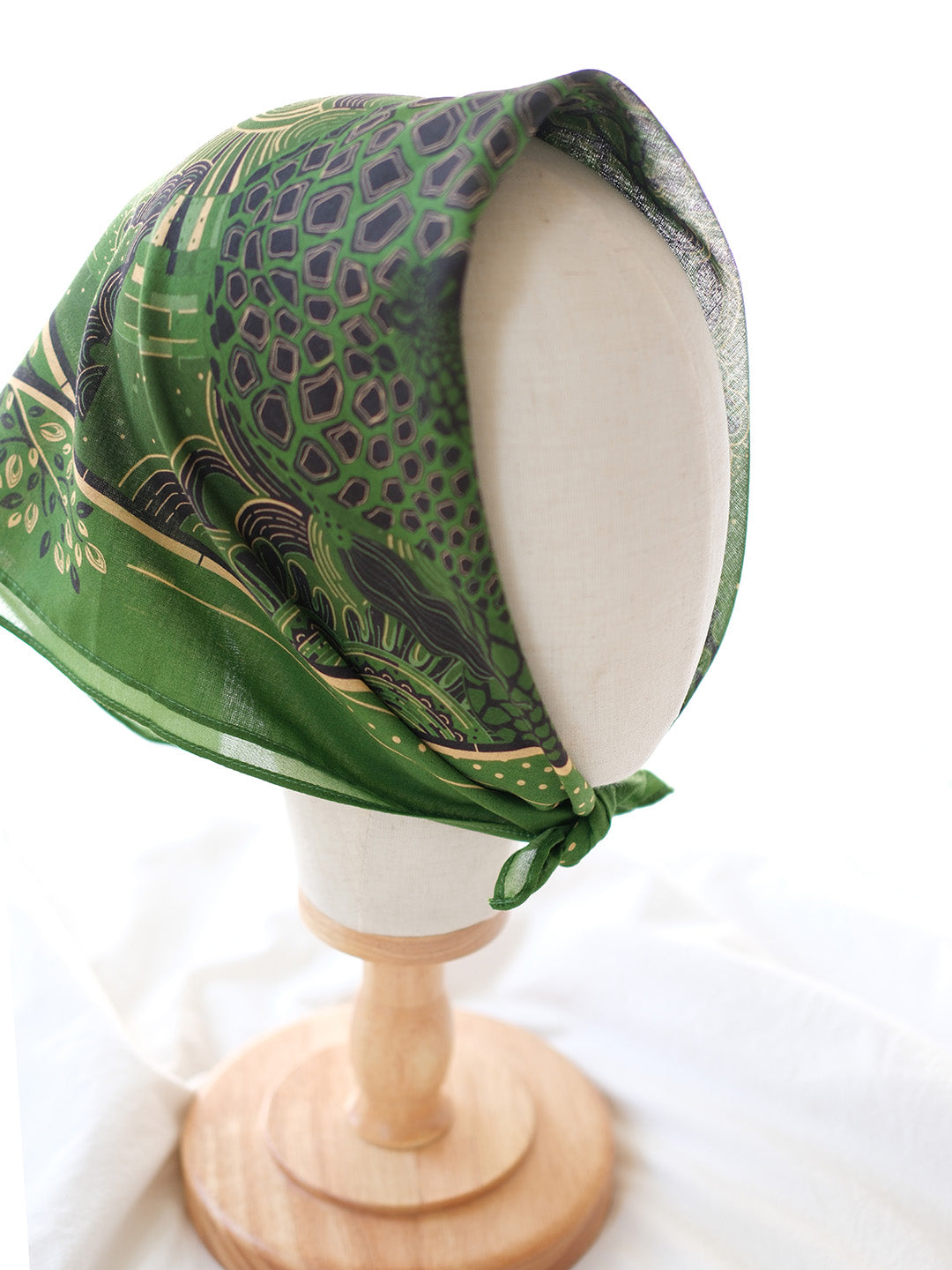 Olive green bandana scarf featuring a giraffe family design, displayed on a wooden mannequin.