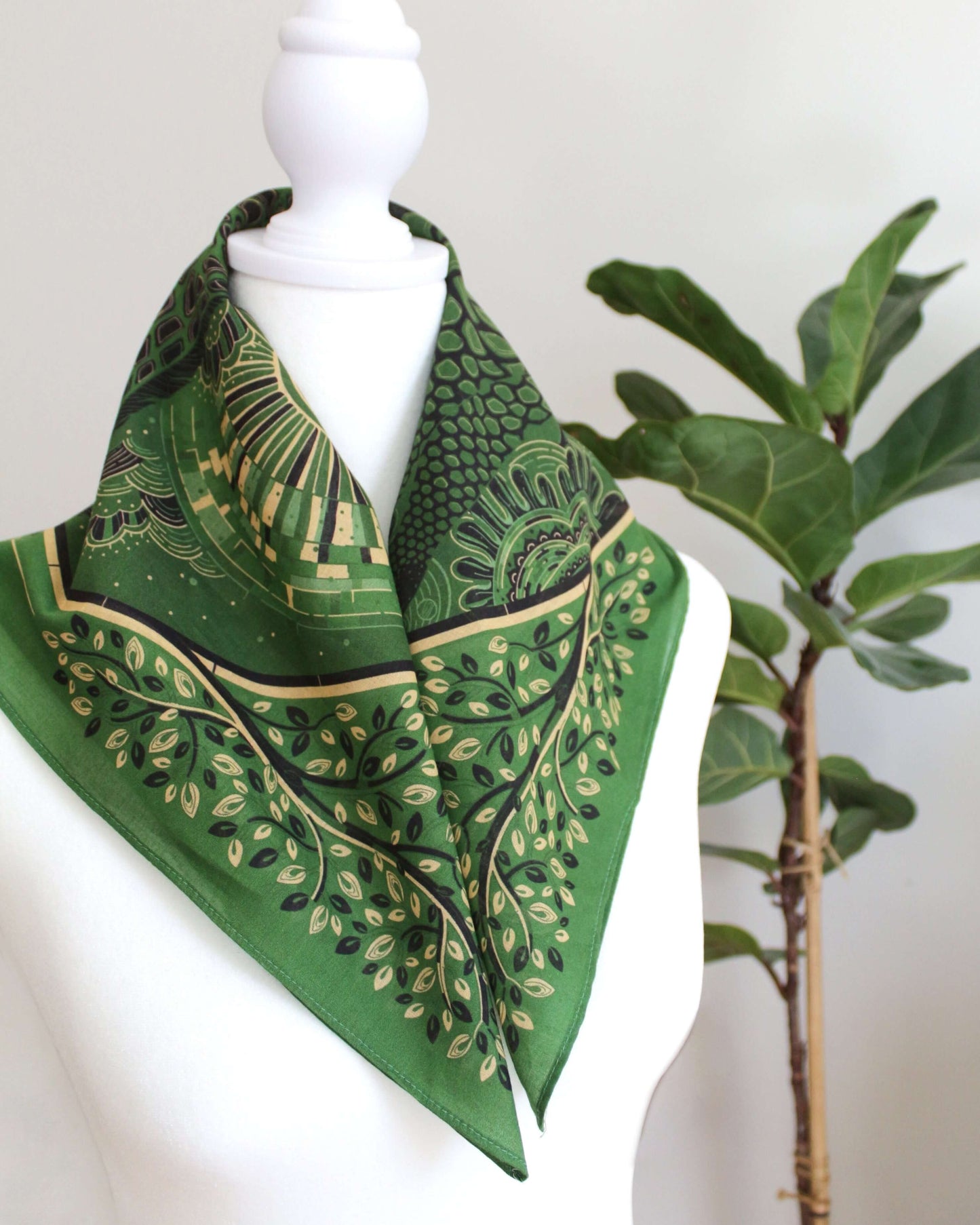 Olive green bandana scarf displayed on a mannequin with floral and nature-inspired designs.