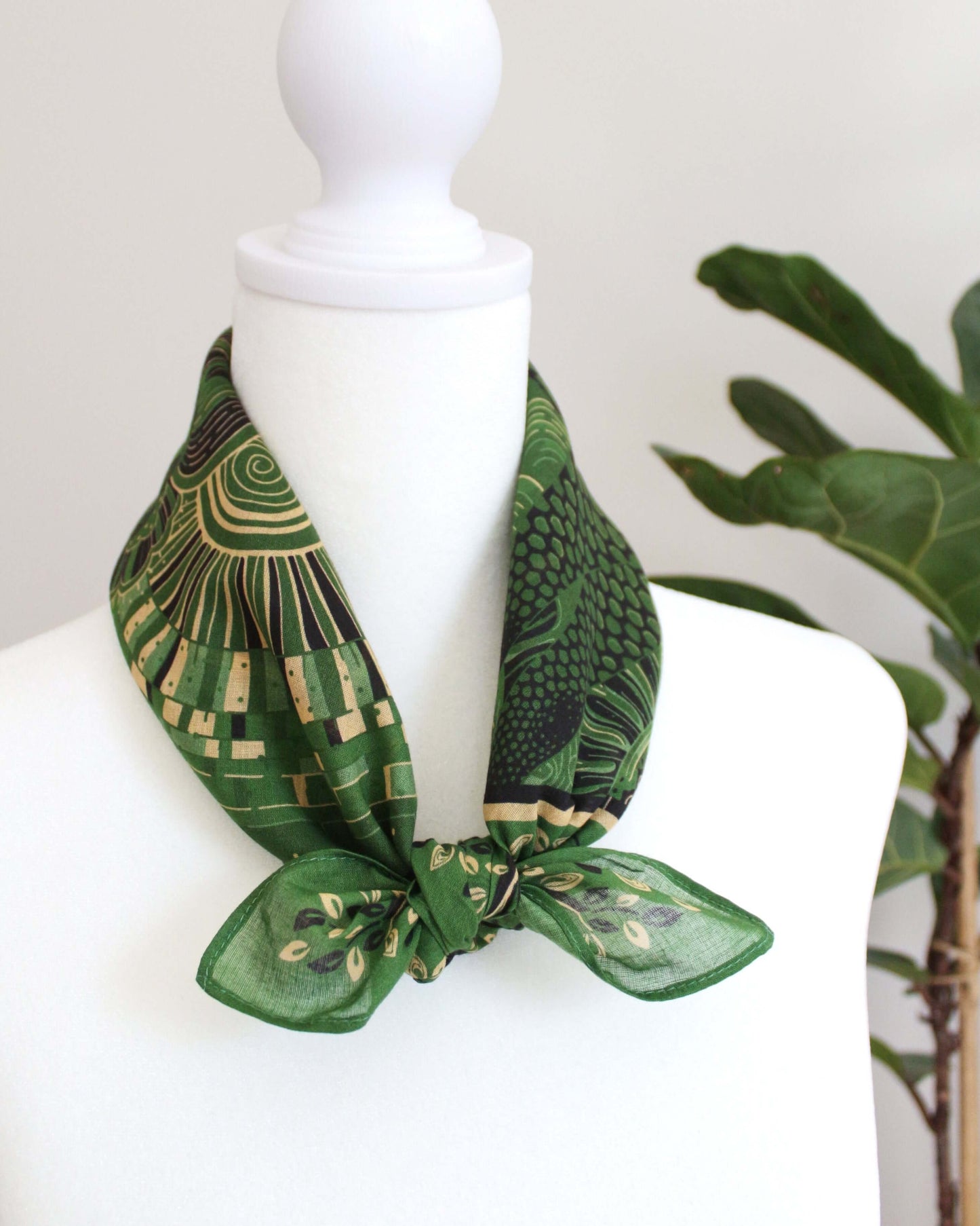 Olive green bandana scarf tied around a mannequin neck, featuring colorful patterned designs.