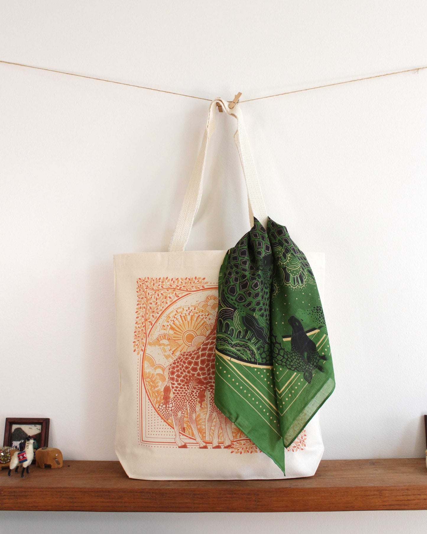 Stylish canvas tote bag with intricate orange design and green patterned scarf hanging on it.