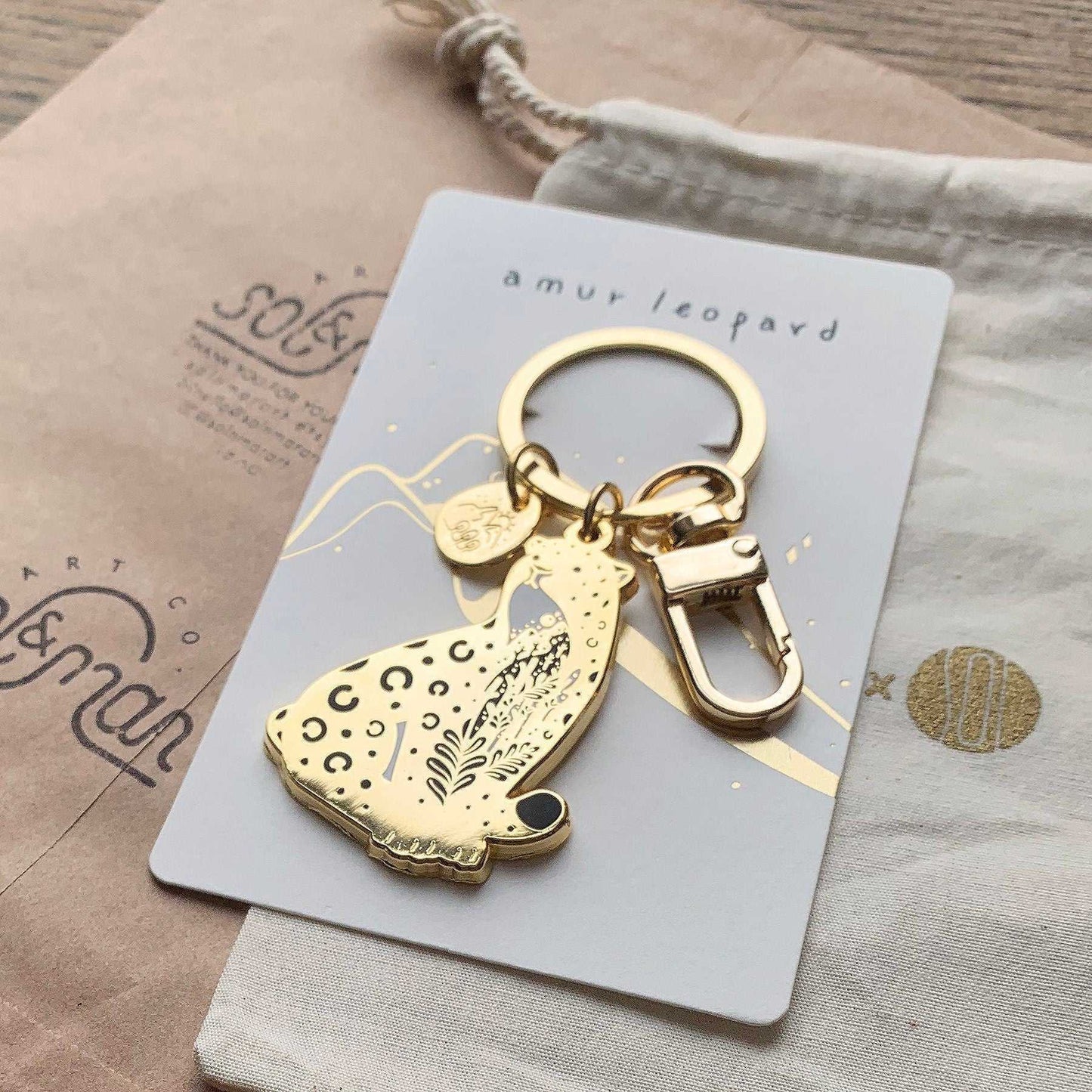 Gold Amur Leopard enamel keychain on display card highlighting its endangered status, featuring habitat art and charm.