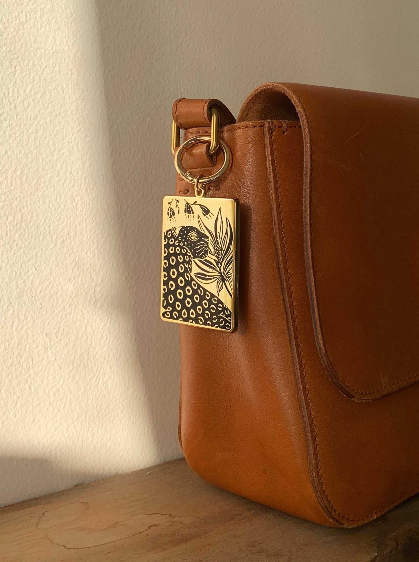 Leopard and Flowers enamel keychain attached to a stylish brown leather purse.