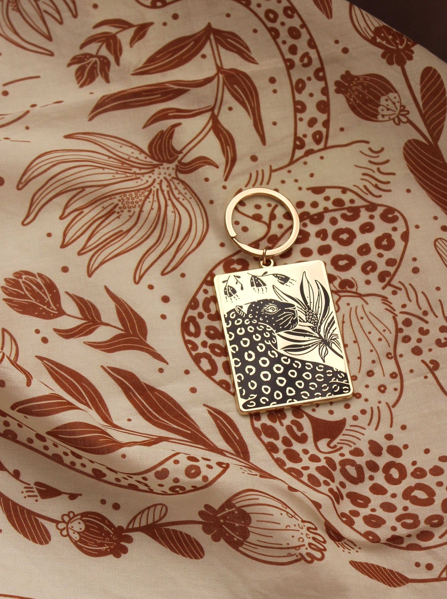 Leopard and flowers enamel keychain on a floral patterned background, featuring gold-plated metal and hard enamel design.