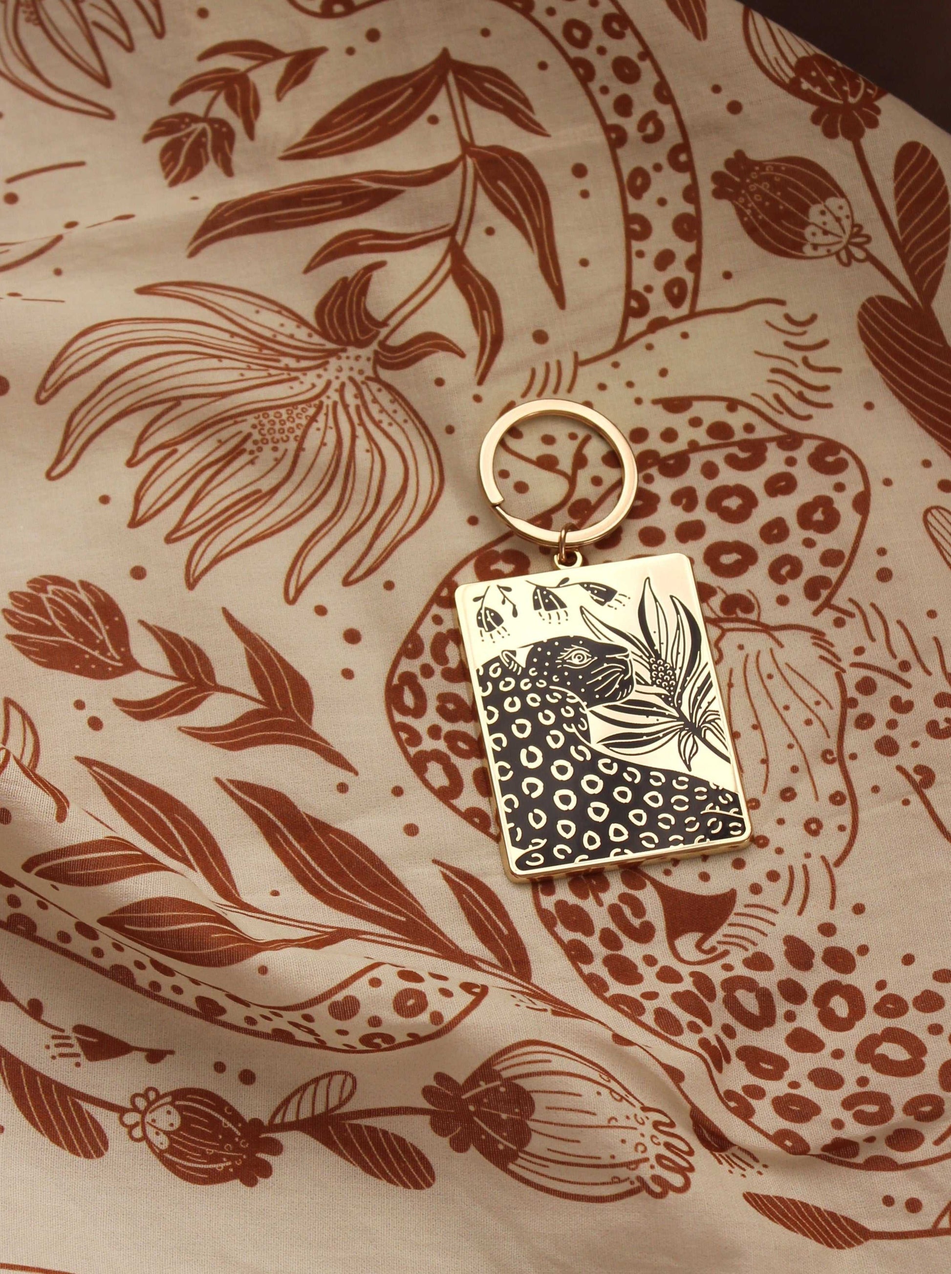 Leopard and flowers enamel keychain on a floral patterned background, featuring gold-plated metal and hard enamel design.