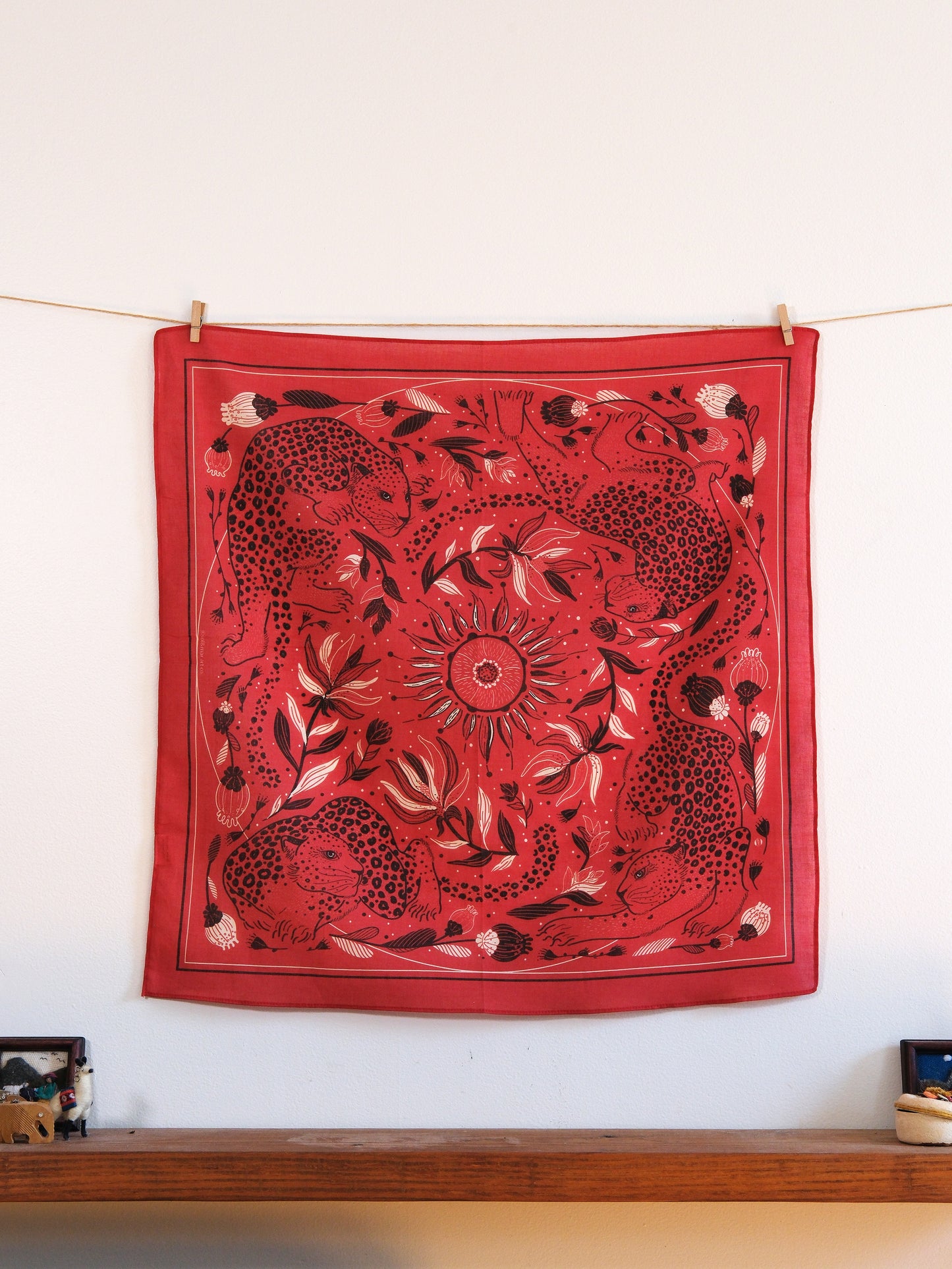 Red bandana with black and white patterns hanging on a line against a white wall.