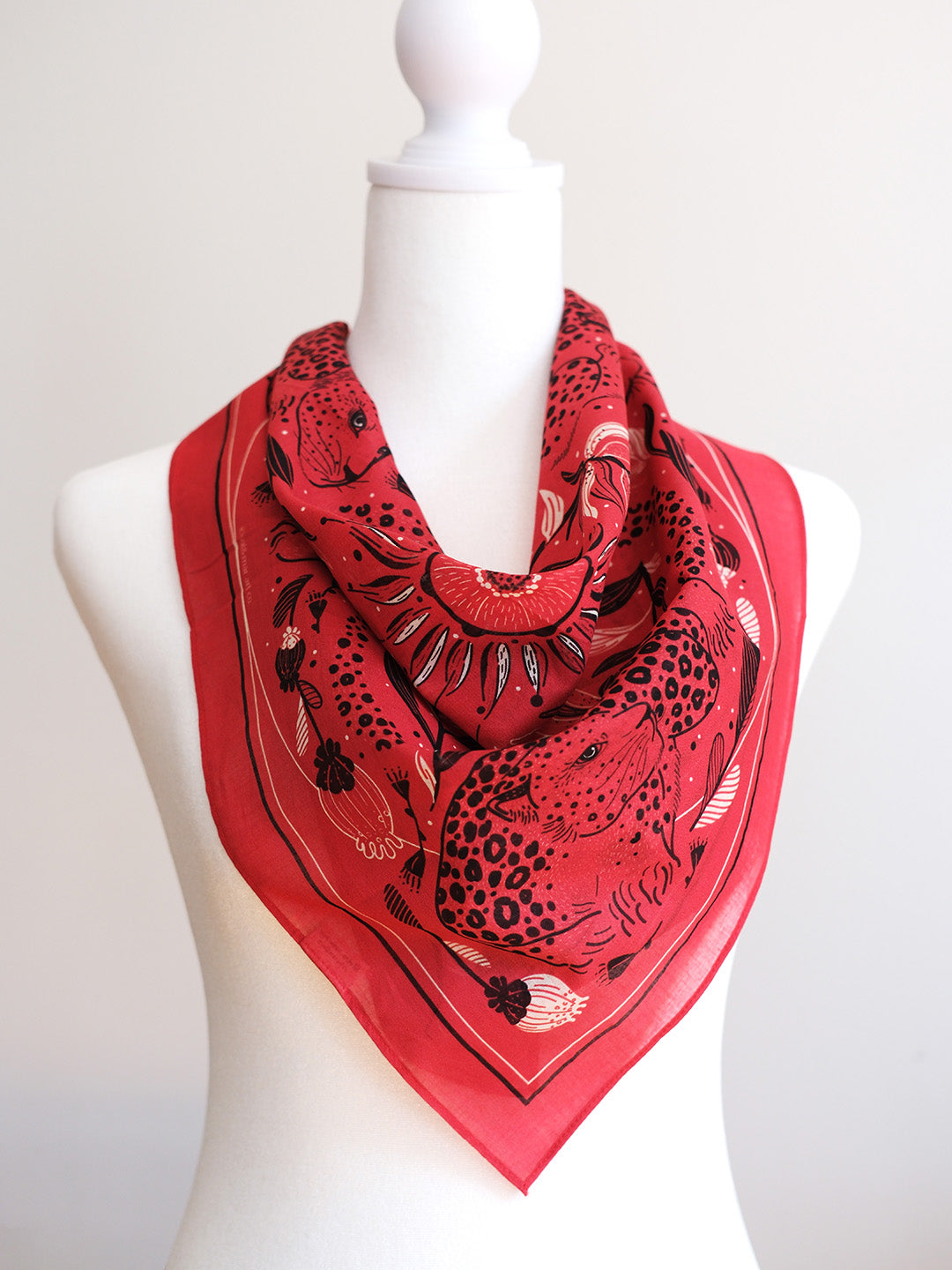 Red scarf with black animal print pattern on a mannequin against a white background