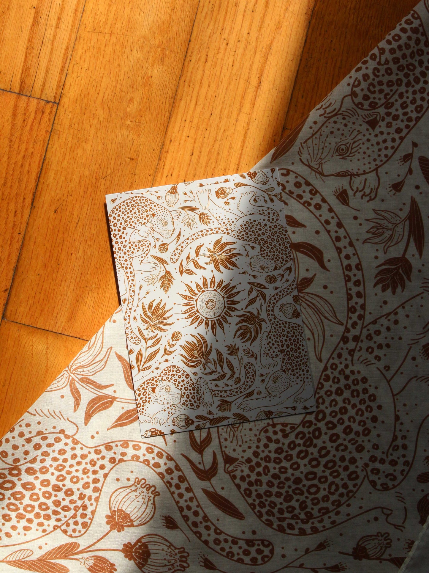 Leopard and Sun bandana scarf in off-white with intricate line art patterns on a wooden surface.