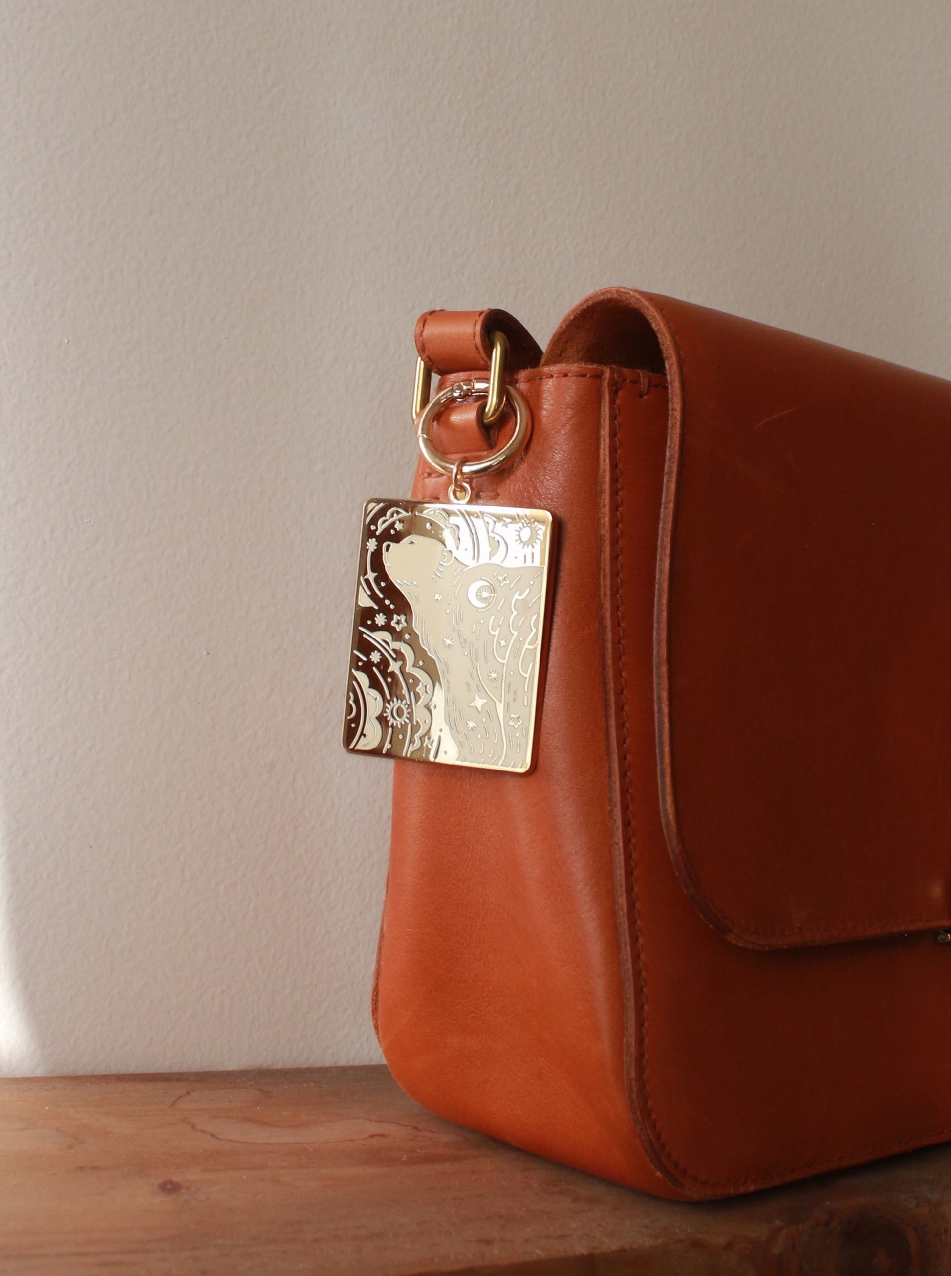 Elegant brown leather handbag with a gold-plated charm attached, showcasing a stylish design.