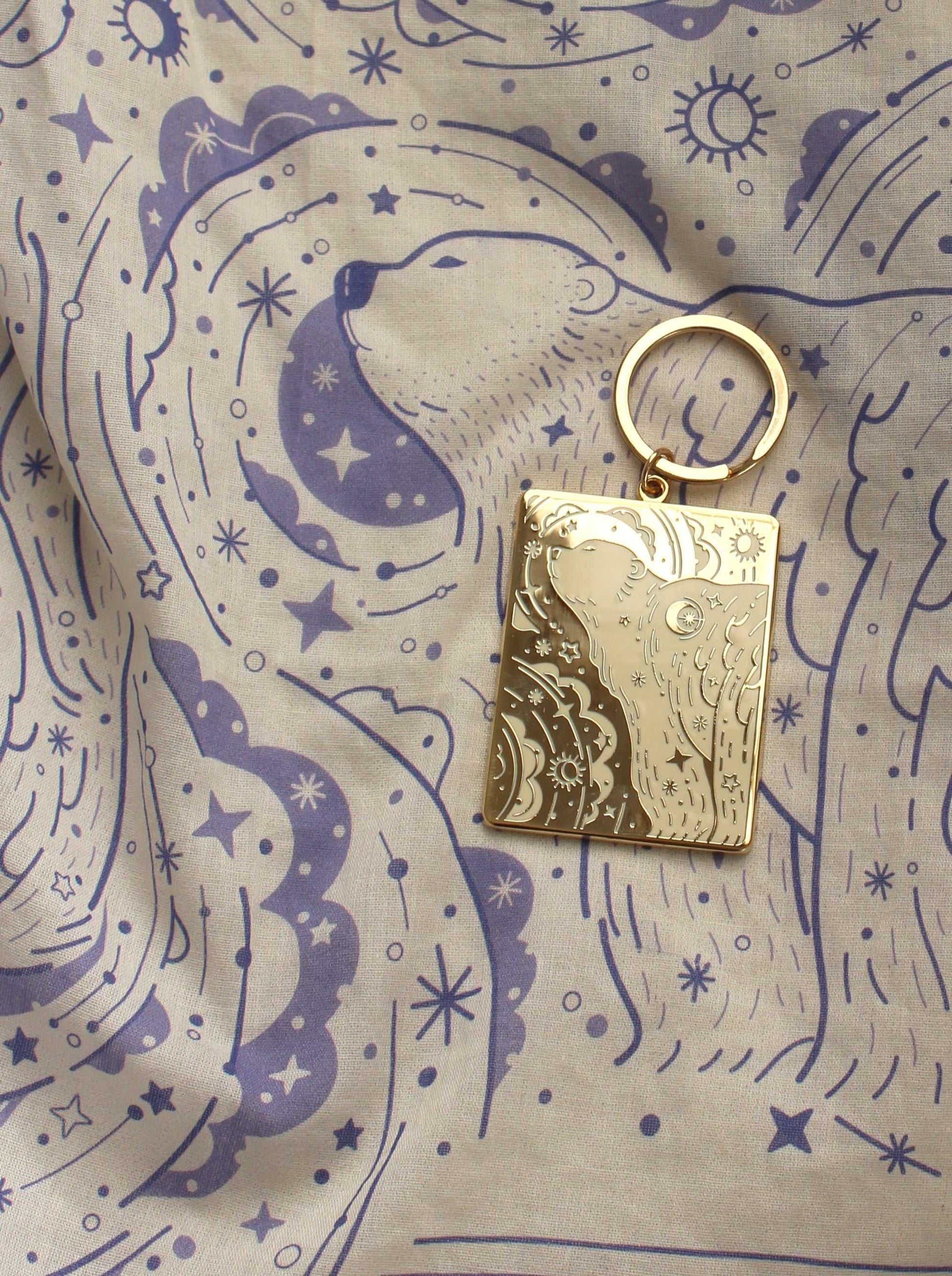 Polar Bear and Northern Sky enamel keychain on a patterned fabric background featuring stars and swirls.