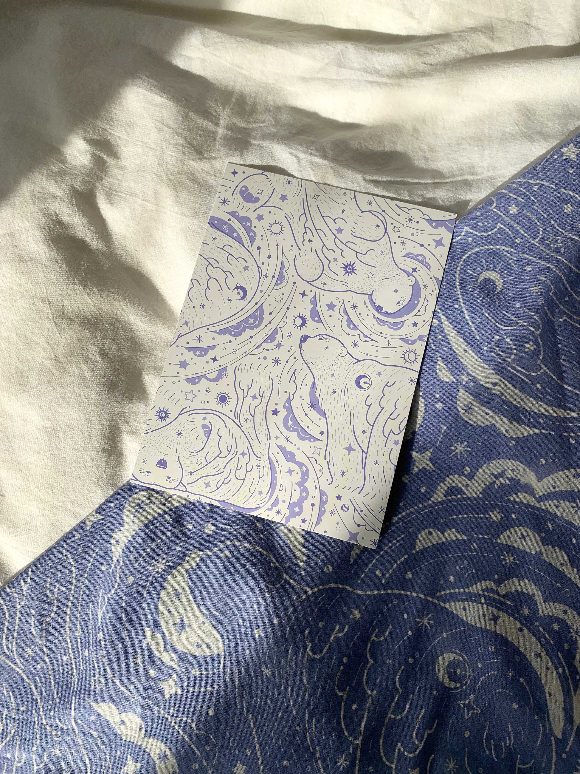 Whimsical illustration on a card atop textured blue and white fabric, showcasing abstract designs and celestial motifs.