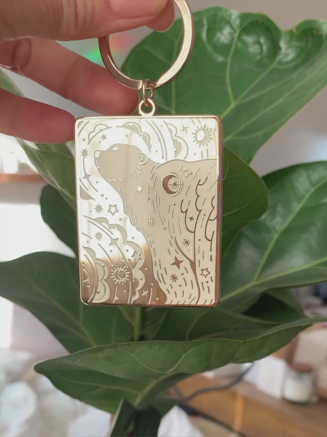 Gold-plated enamel keychain featuring a polar bear and northern sky design, attached to a green plant.
