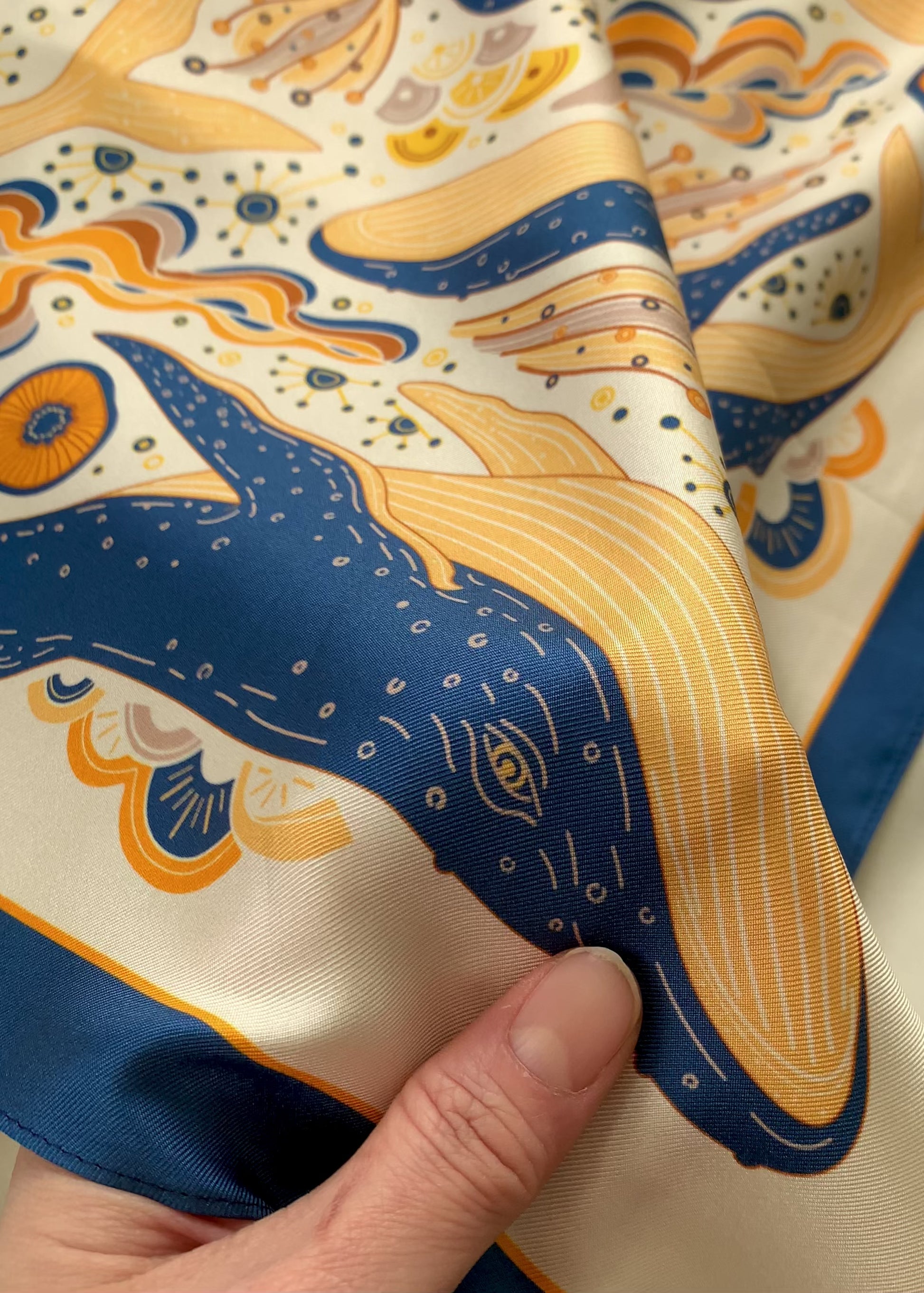 Hand holding a colorful silk twill scarf featuring an illustrated Humpback Whale design.