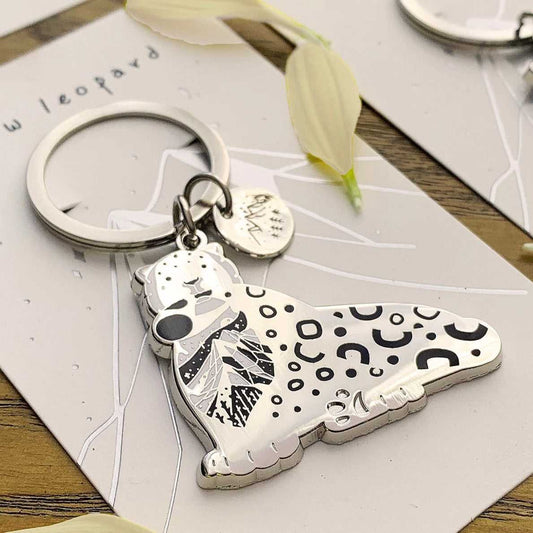 Snow Leopard enamel keychain featuring intricate habitat art and an organic-shaped round tag.