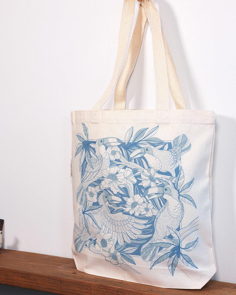 Tote bag with blue floral design hanging on a wooden shelf against a white wall.