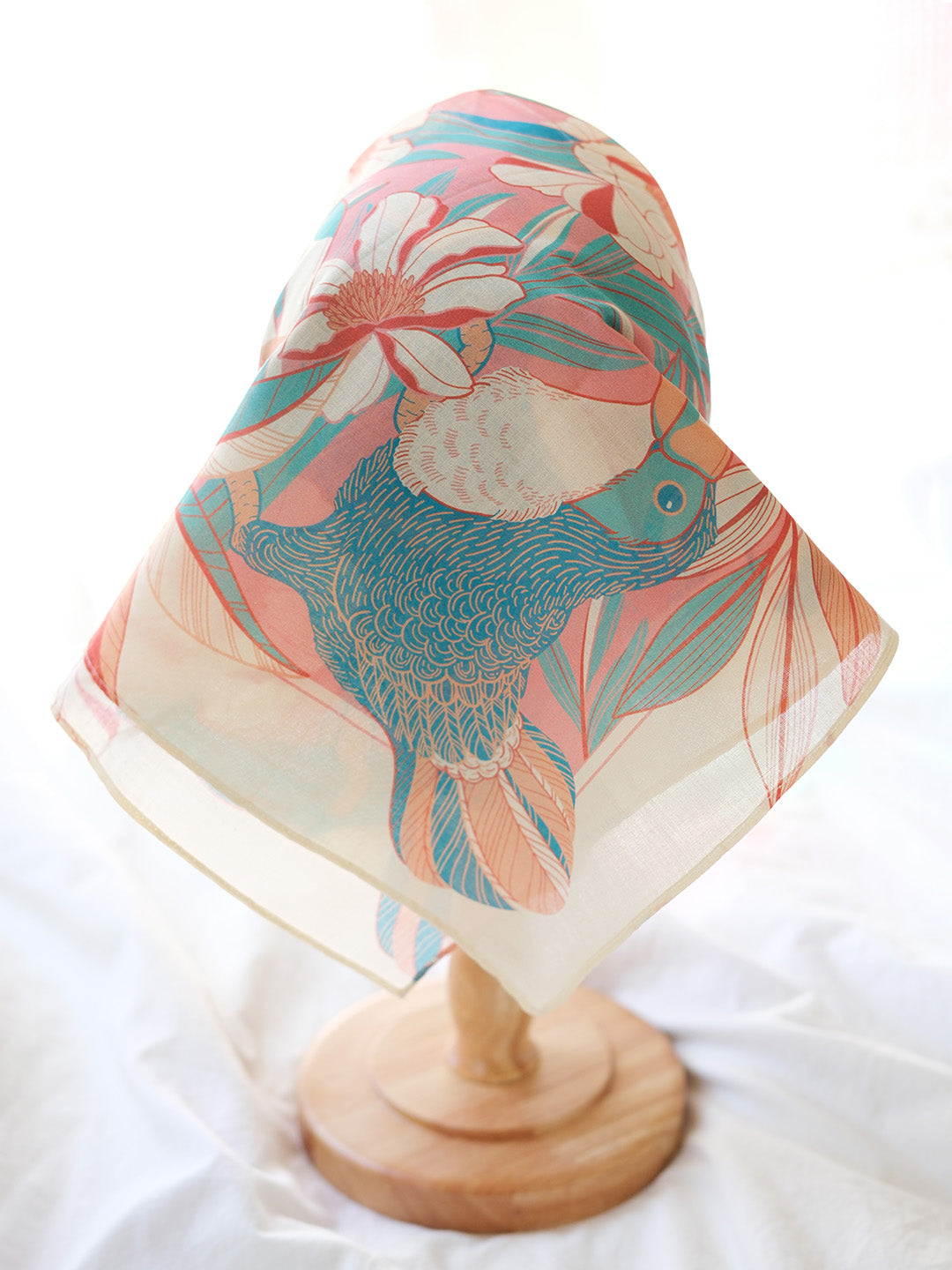 Toucan in a floral design bandana scarf displayed on a wooden stand, showcasing vibrant colors and soft fabric.