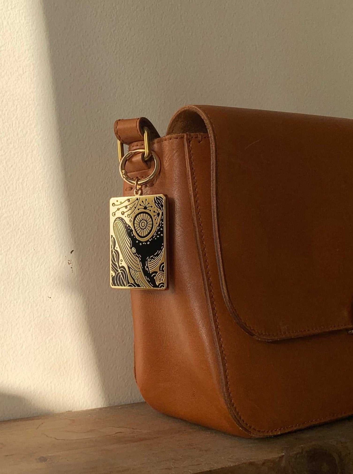 Humpback whale and ocean enamel keychain attached to a stylish brown handbag.