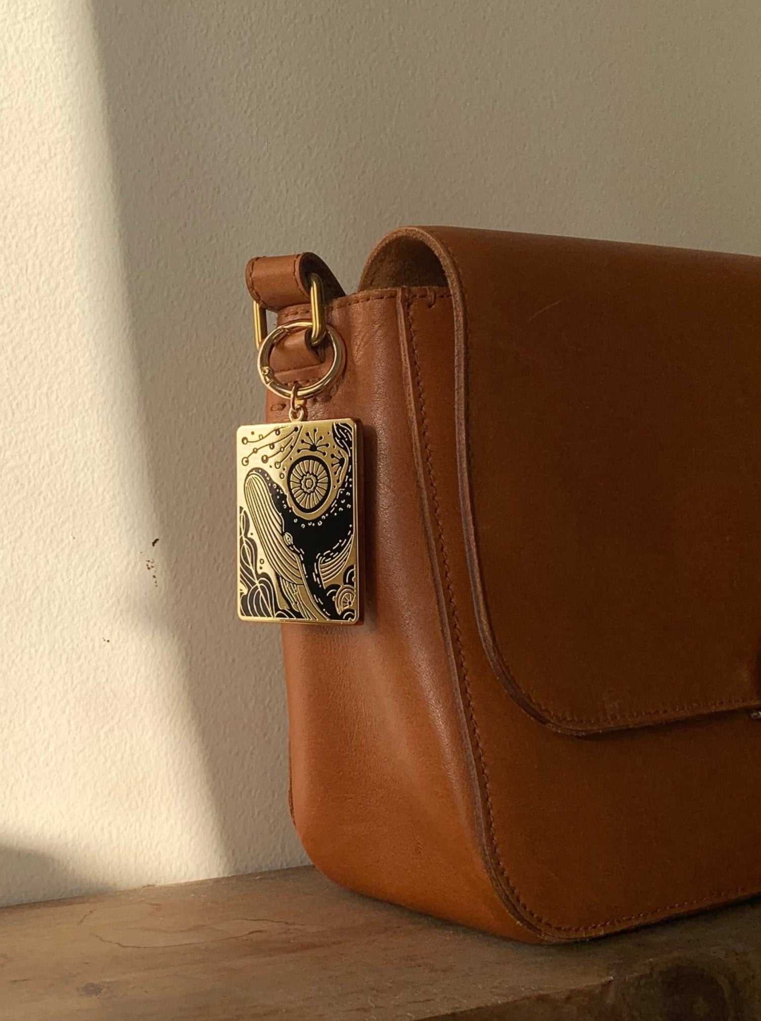 Humpback whale and ocean enamel keychain attached to a stylish brown handbag.