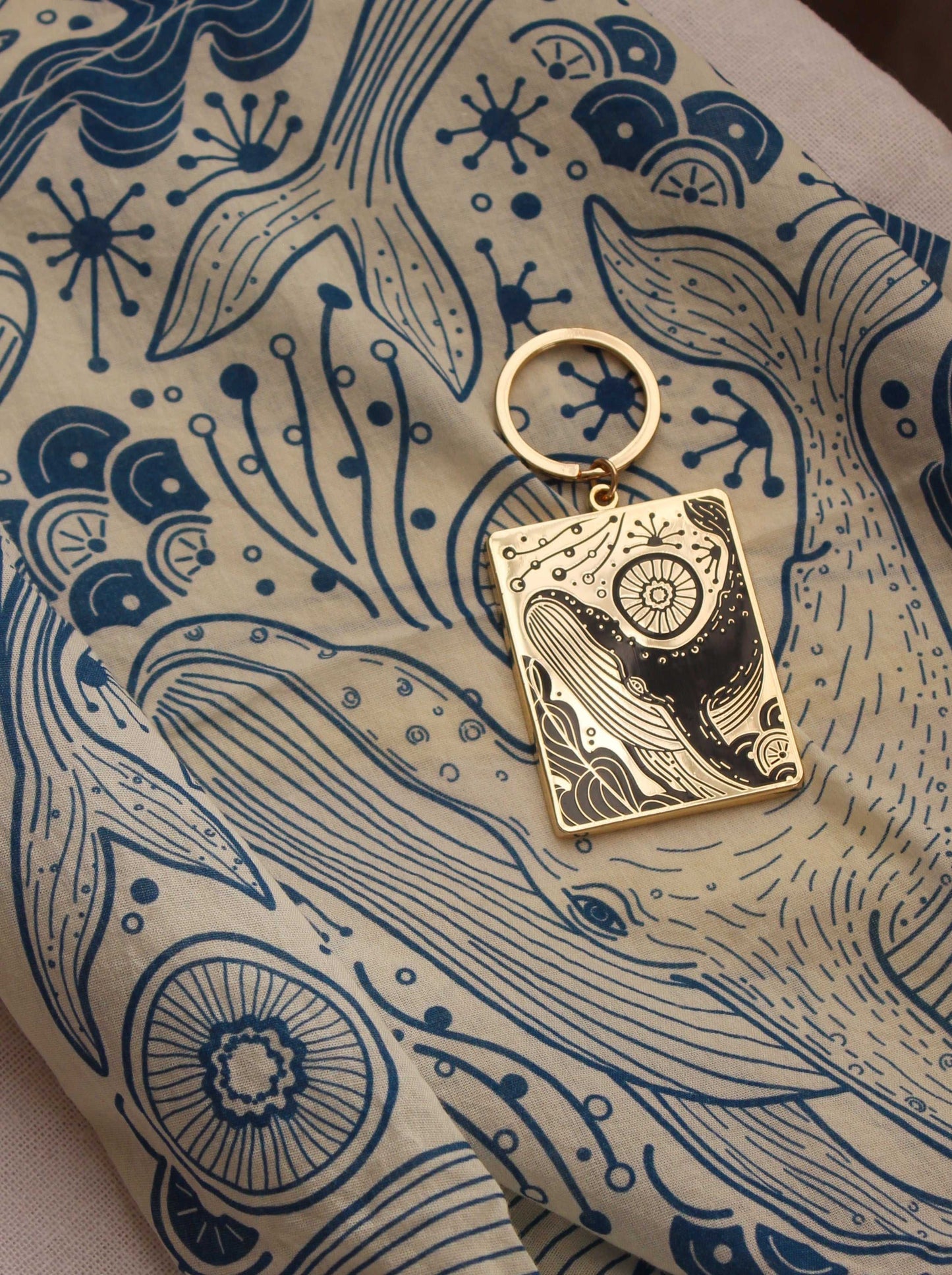 Humpback whale enamel keychain on a patterned fabric, showcasing ocean-themed illustrations.
