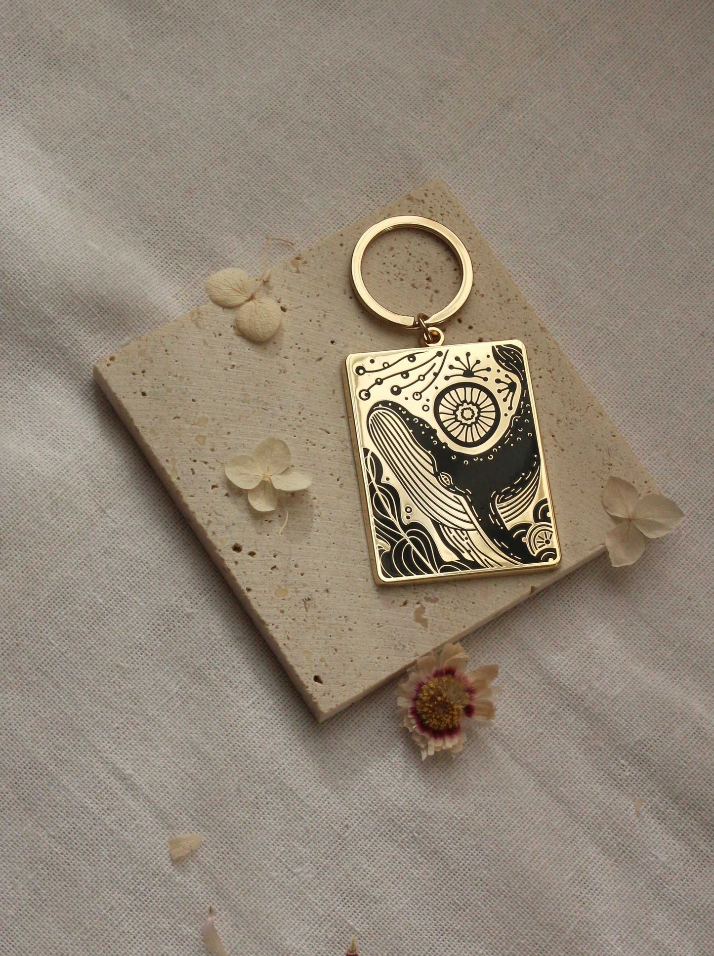 Humpback whale enamel keychain with ocean design on textured background, gold plated metal, artful illustration.