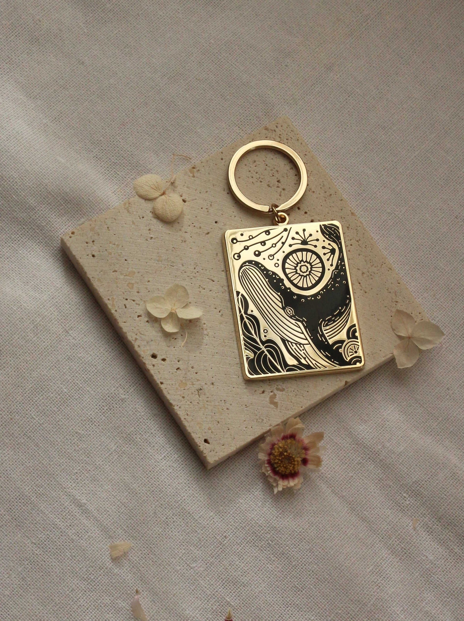 Humpback whale enamel keychain with ocean design on textured background, gold plated metal, artful illustration.
