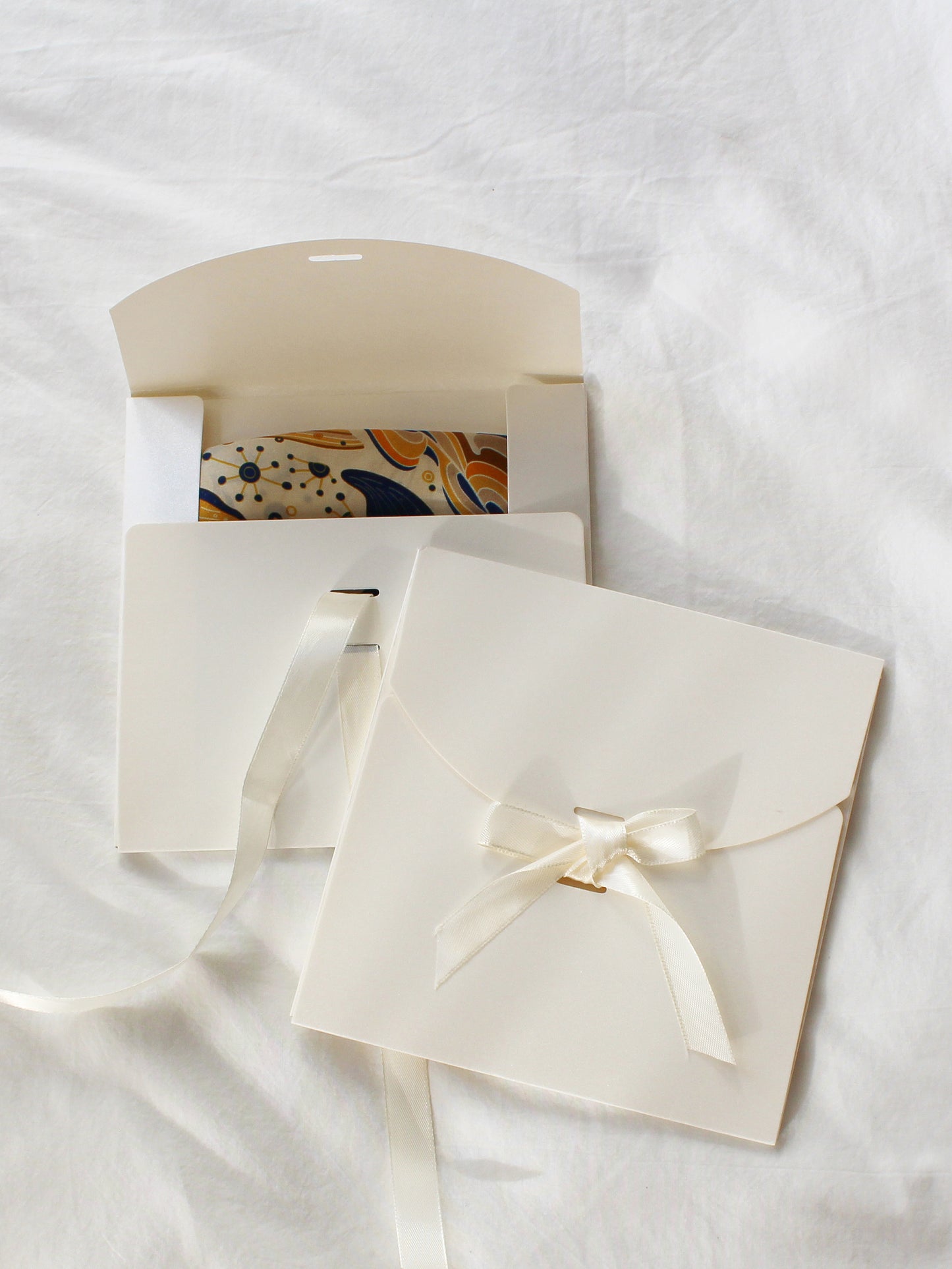 Elegant white envelopes with a ribbon, one partially open revealing a colorful patterned card inside.