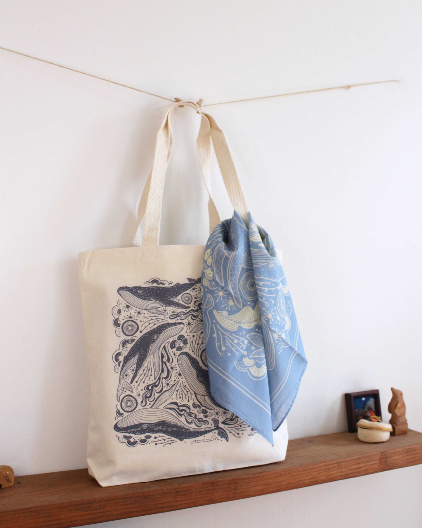Whale and ocean art canvas tote bag with blue scarf displayed on a wooden shelf.