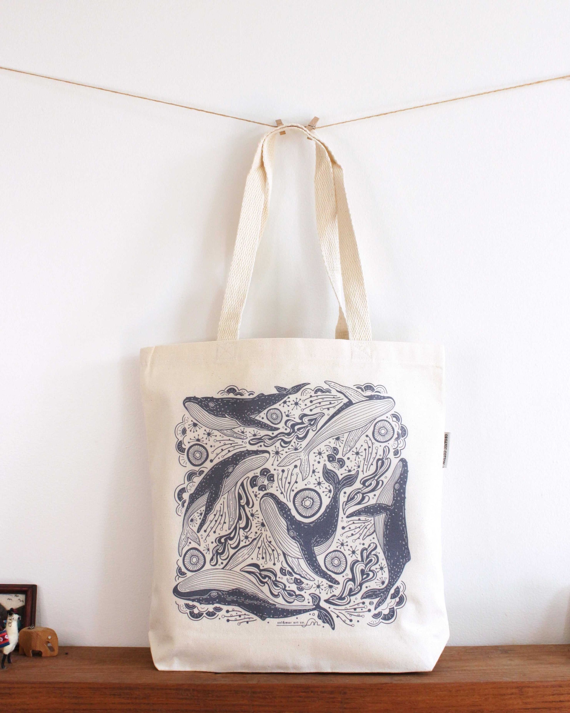 Whale and ocean illustrated canvas tote bag on display with sturdy handles, perfect for everyday use.
