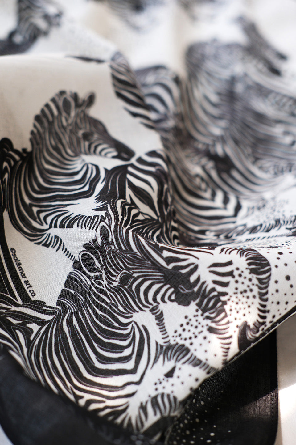 Close-up of a black and white bandana scarf featuring an artistic illustration of zebras.