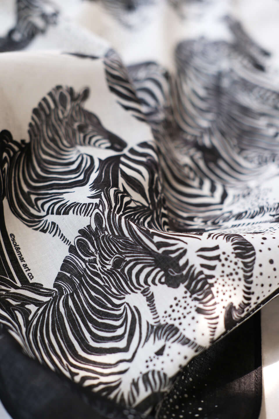 Close-up of a black and white bandana scarf featuring an artistic illustration of zebras.