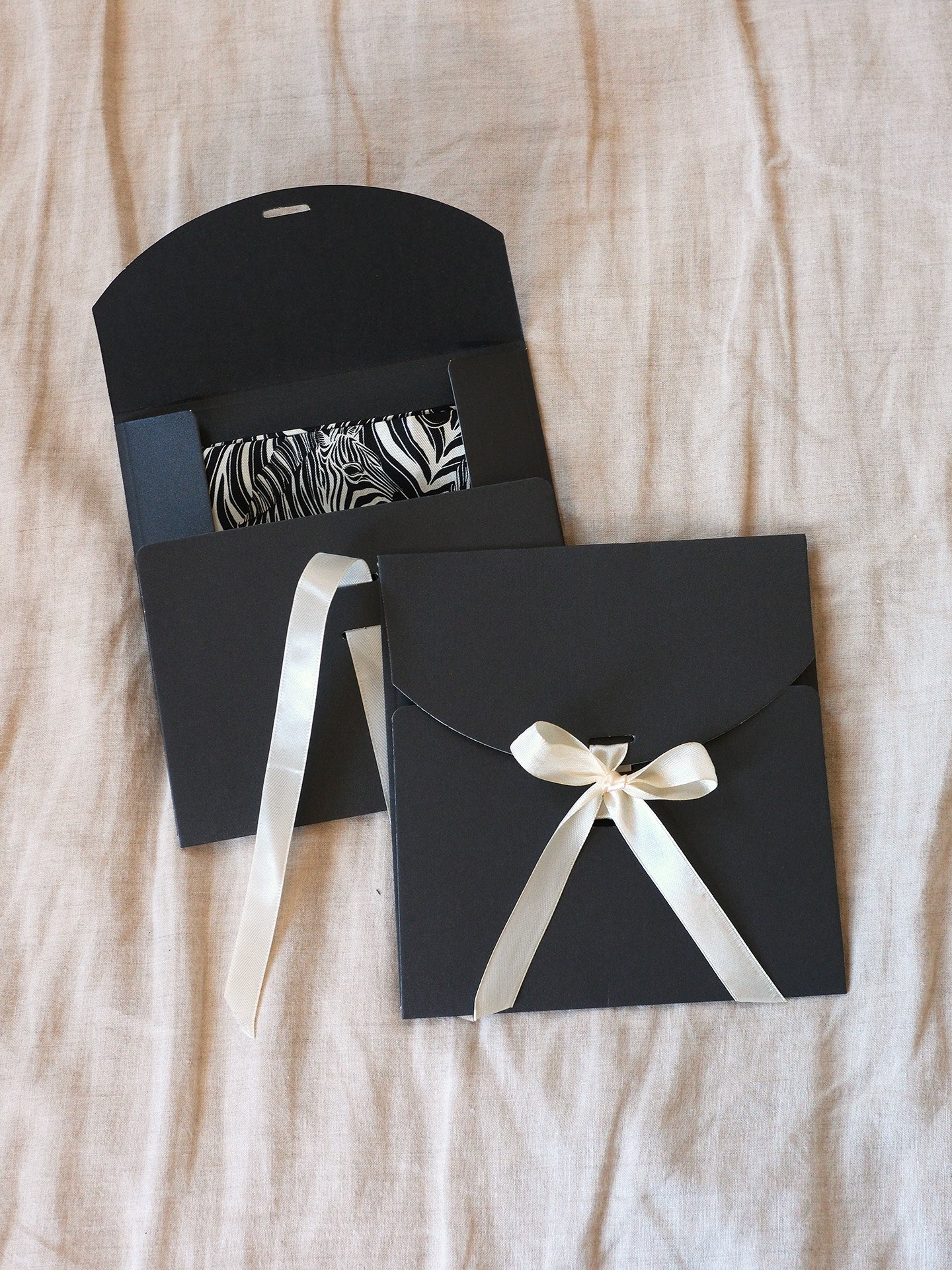 Black envelopes with white ribbons on a beige fabric background