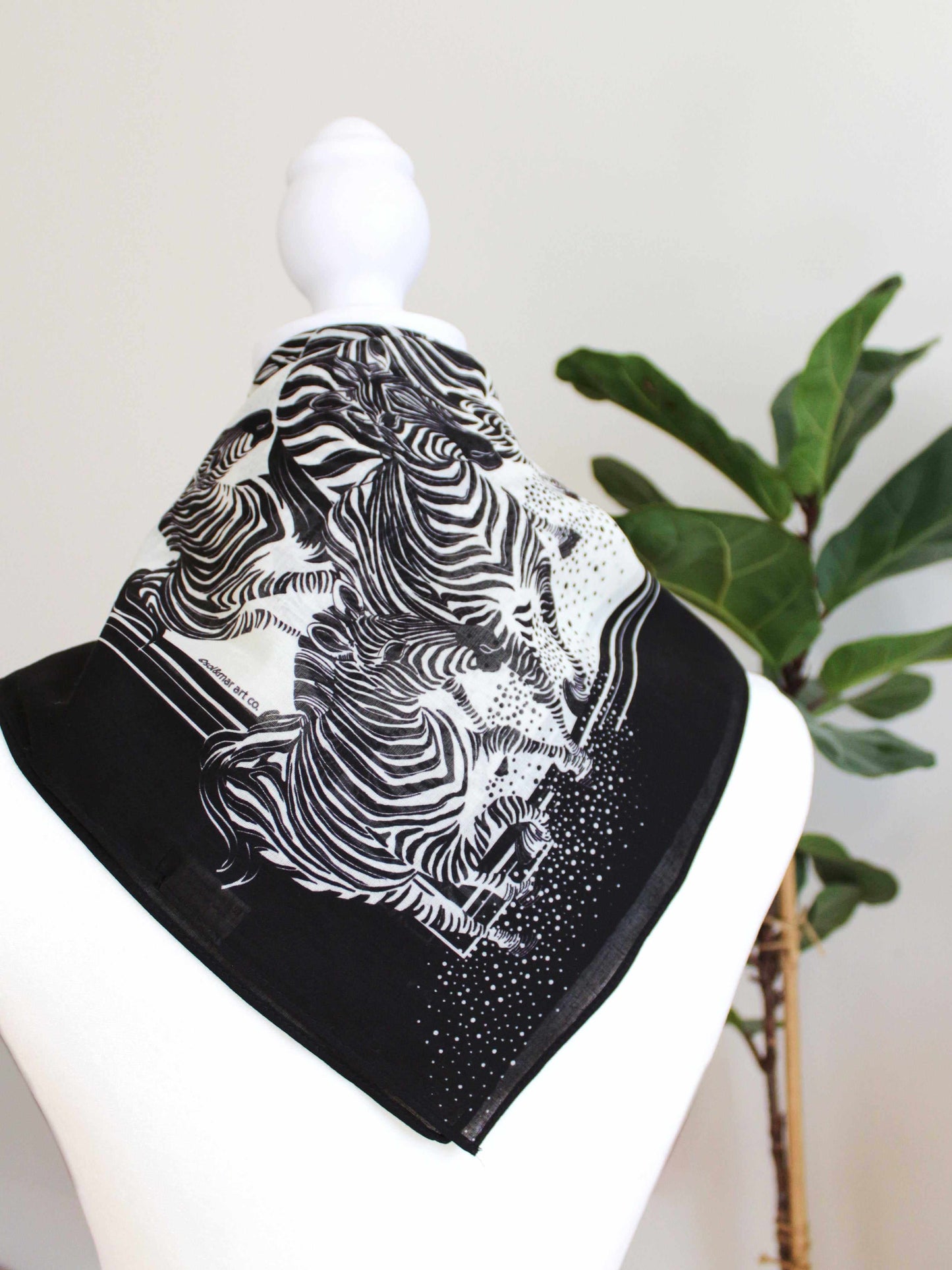 Black and white zebra print bandana scarf displayed on a mannequin with greenery in the background.