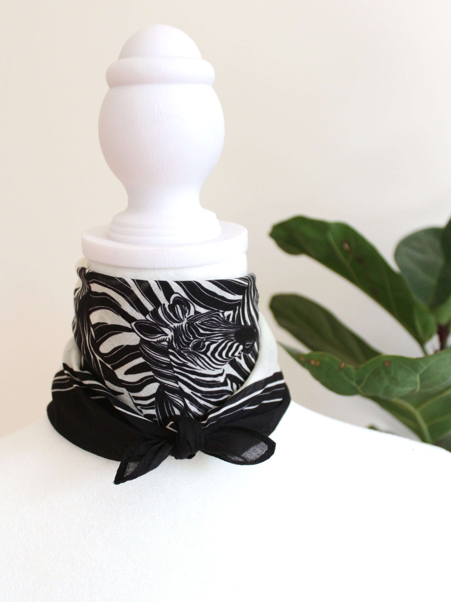 Black and white zebra-patterned bandana scarf tied around a mannequin's neck against a green background.